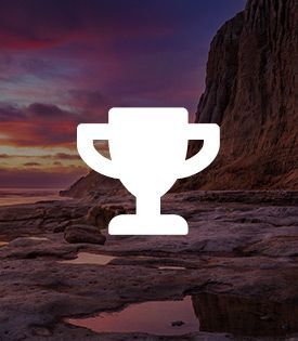 A white trophy icon on a rocky beach with a mountain in the background
