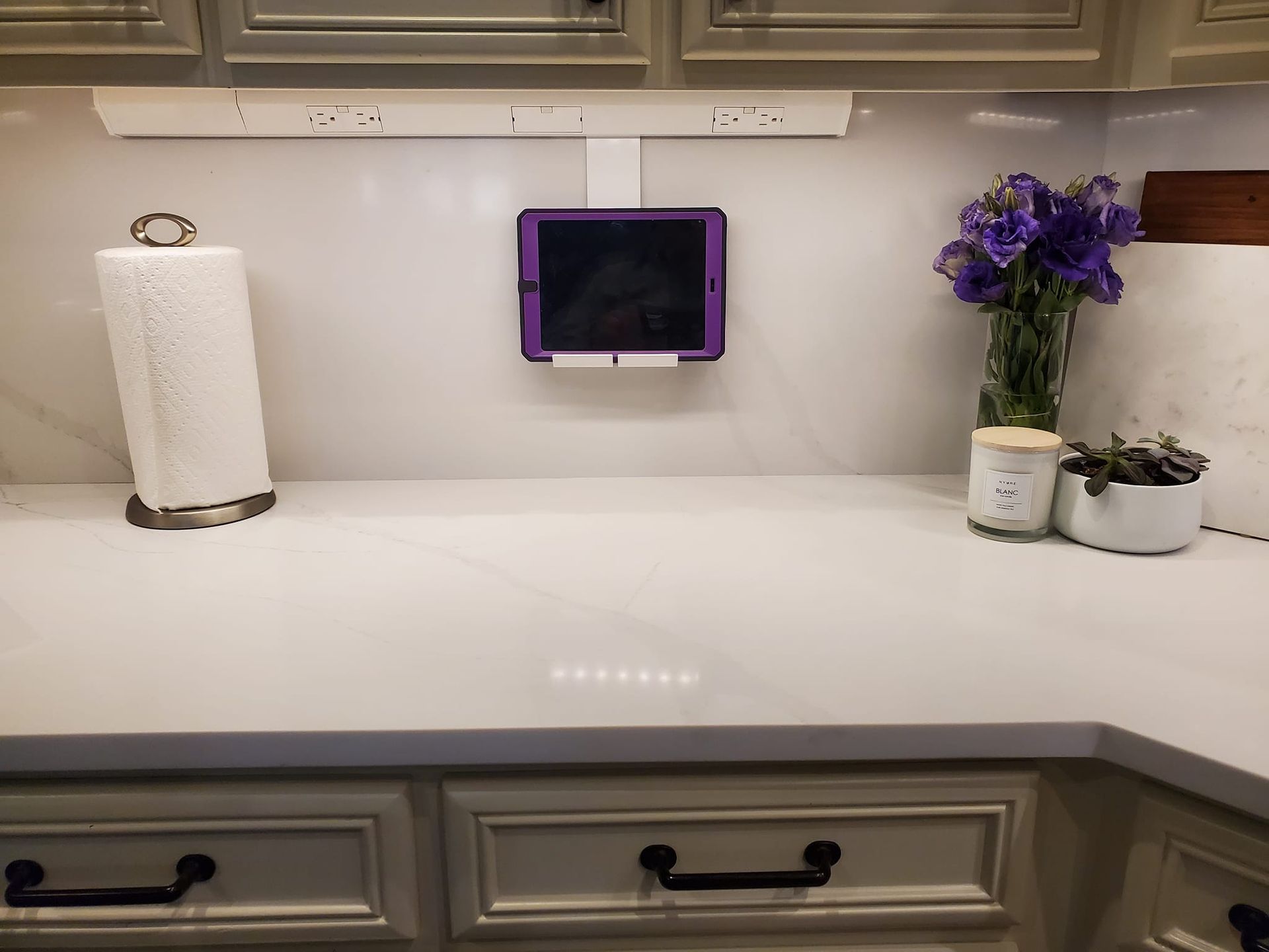 A kitchen counter with a paper towel holder and a tablet mounted to the wall.