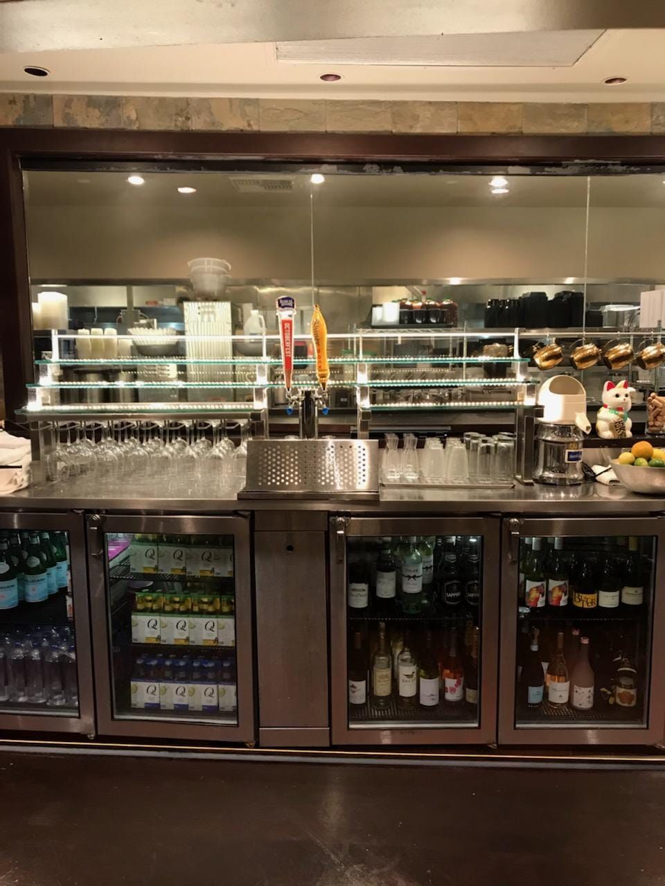 A stainless steel bar in a restaurant with bottles and glasses in it