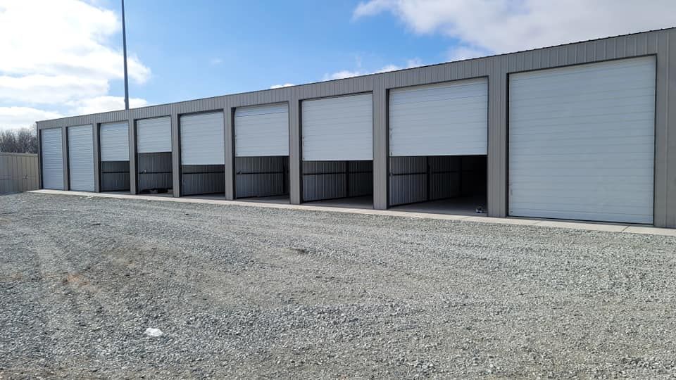 A row of garage doors are open on a gravel road.