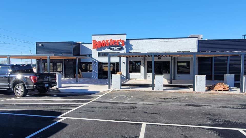 A black truck is parked in front of a rooster 's restaurant.