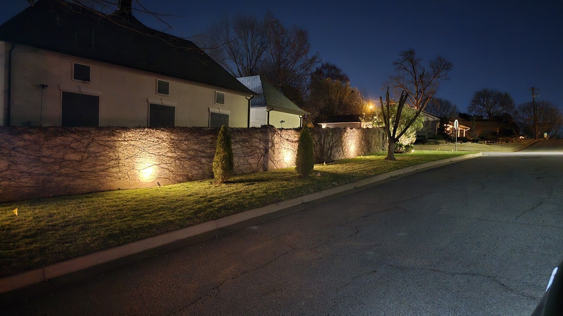 A historic building at night with a long brick wall illuminated by ground-level lights along a quiet road.