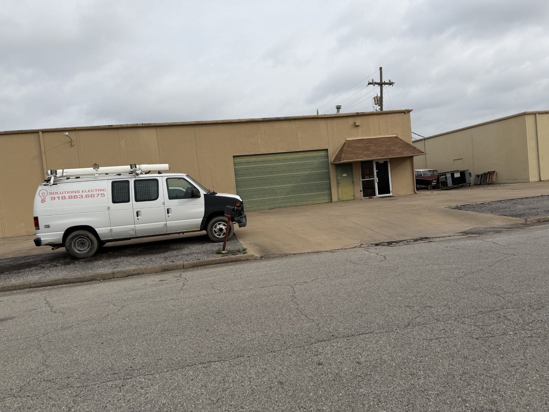 A white service van parked in front of a beige industrial warehouse building with a small entrance under a brown roof.