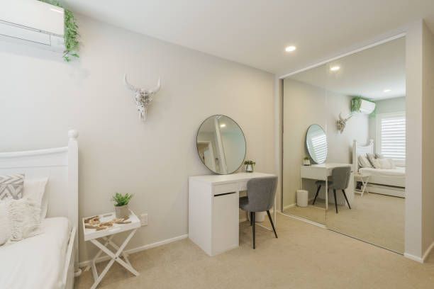 Bedroom with white furniture, including a bed and a vanity. A large mirror reflects the room.