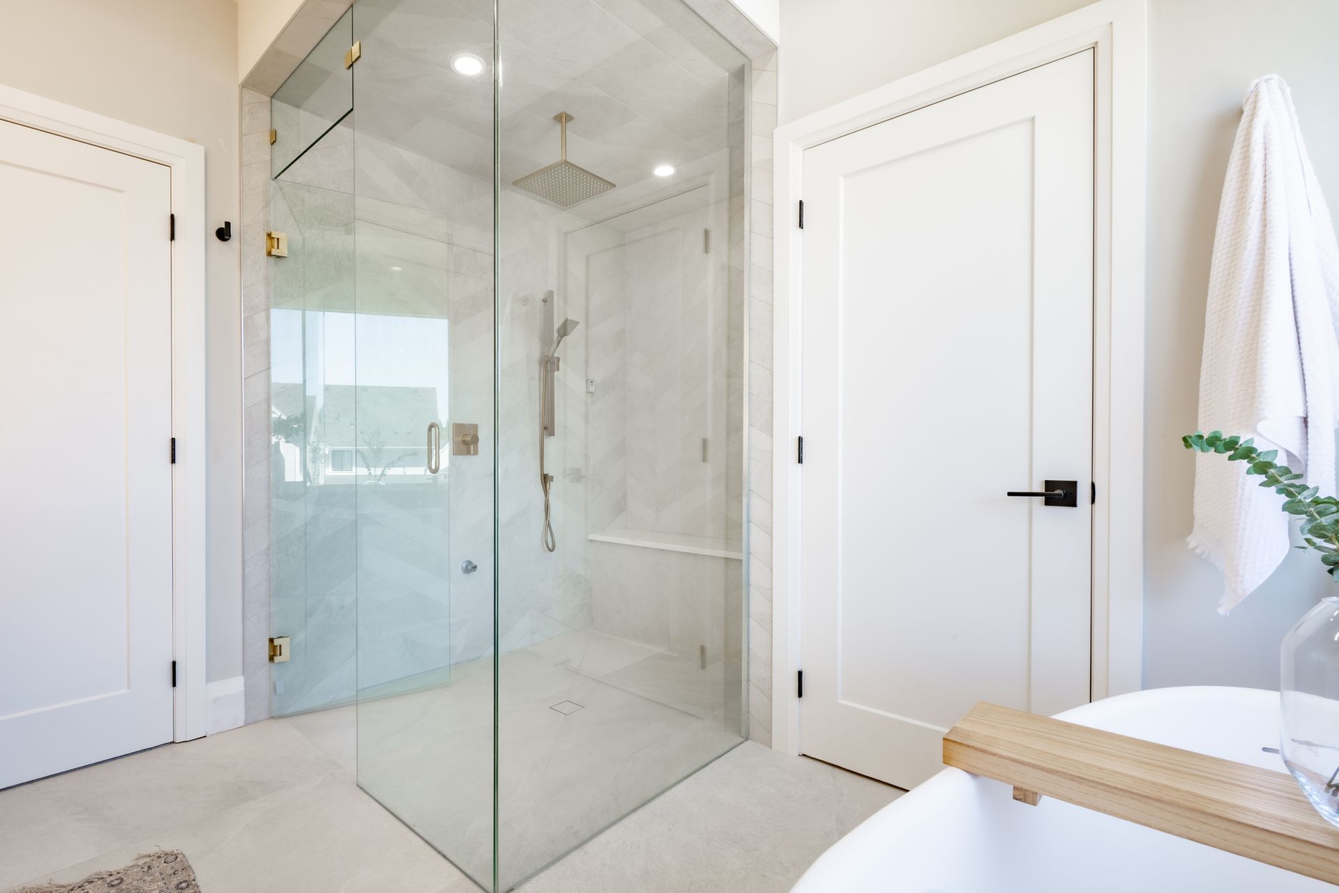 A modern bathroom with a large glass shower, white doors, and a bathtub.