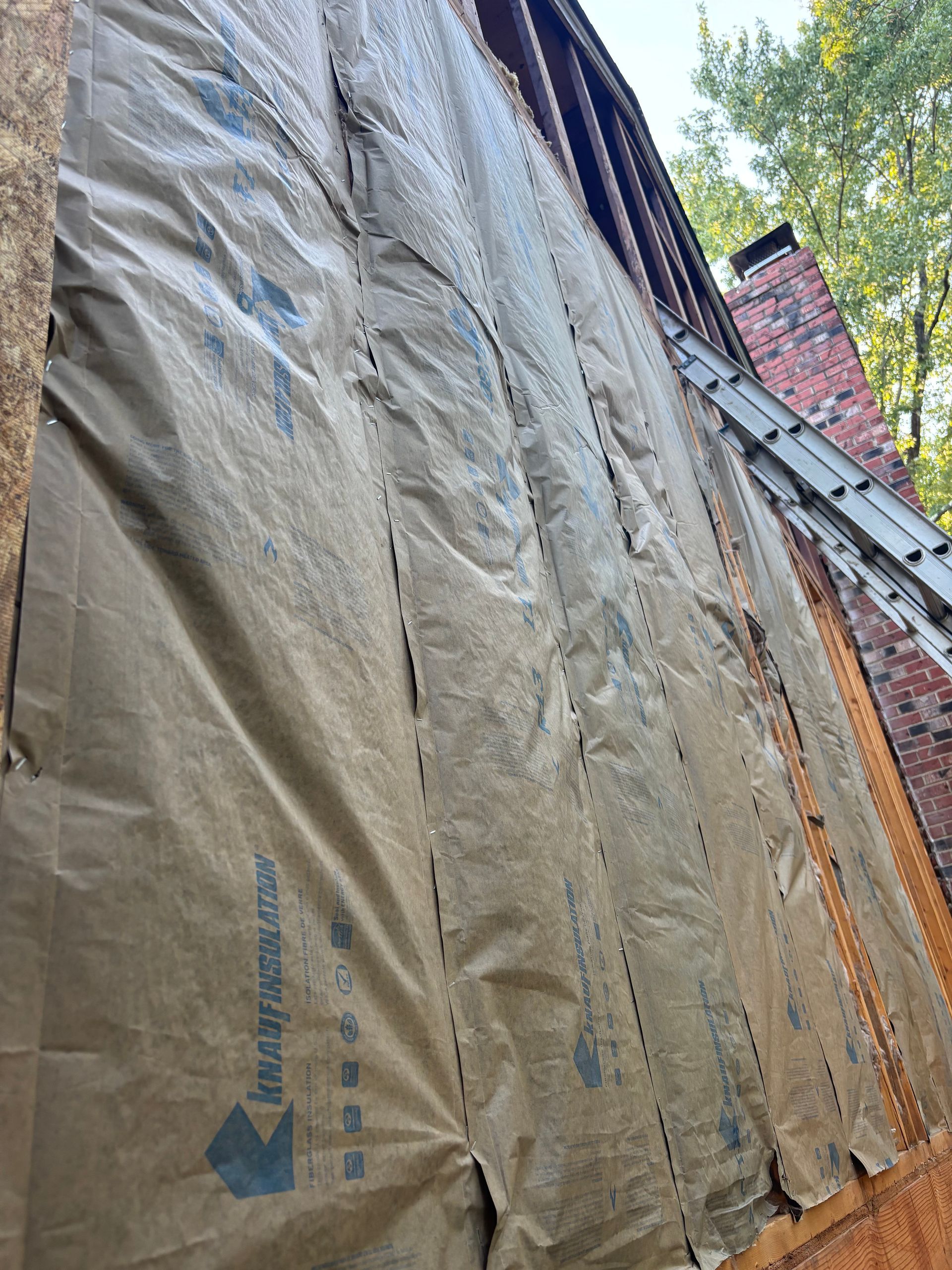 Brown building wrap on a brick wall with a ladder, partially covering the side of a house.