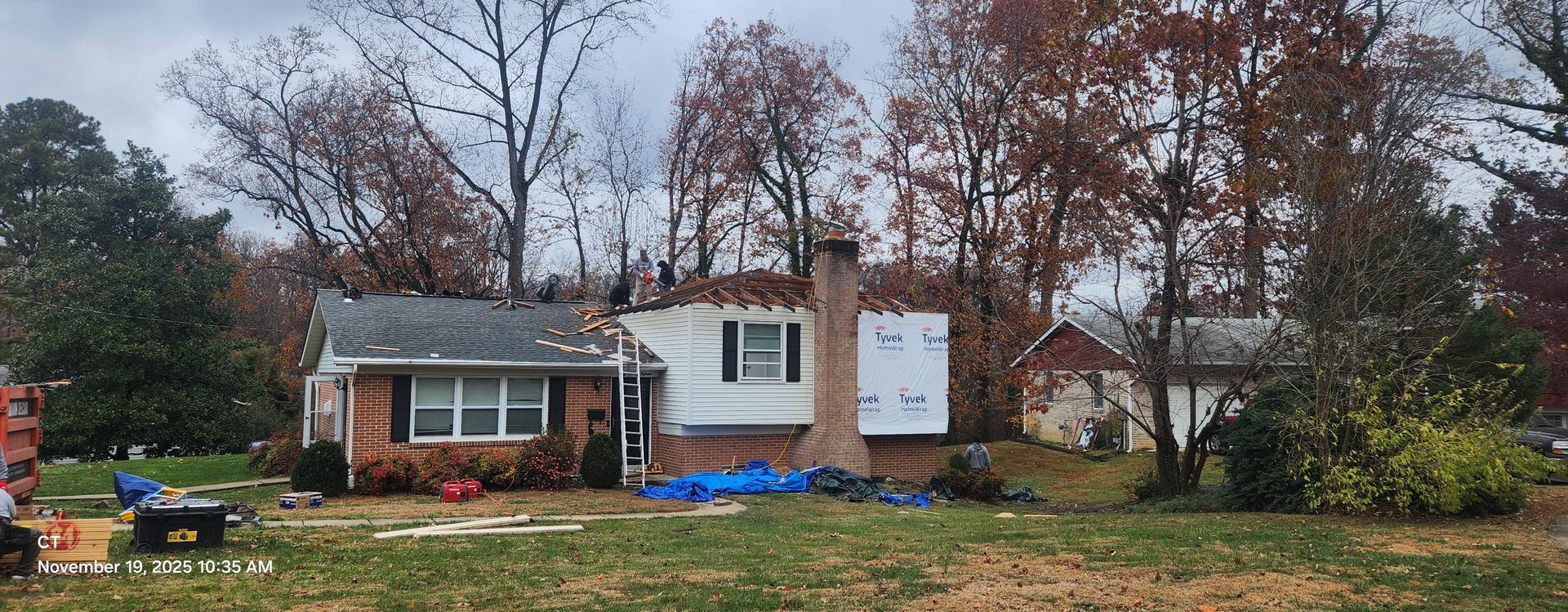 A damaged house with a missing roof, surrounded by trees and debris.