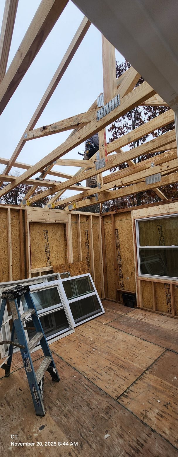 Interior of a building under construction, featuring wooden framing, windows, and a ladder.