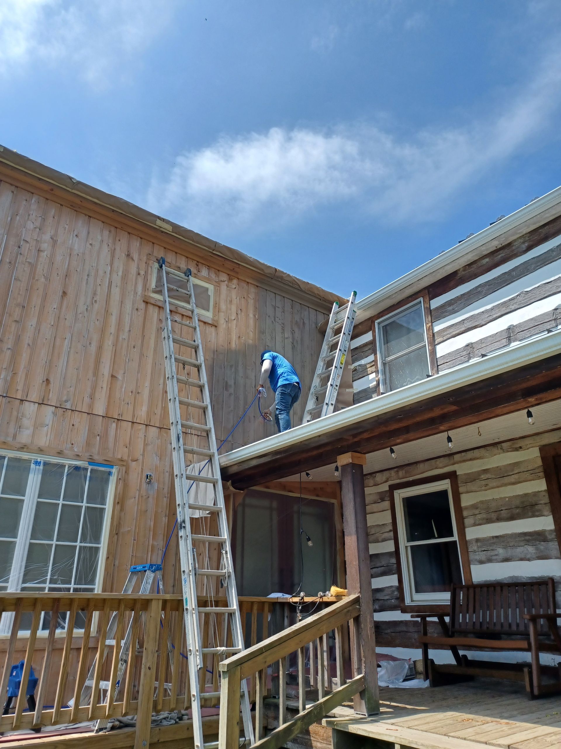A man is painting the side of a log cabin with a ladder.