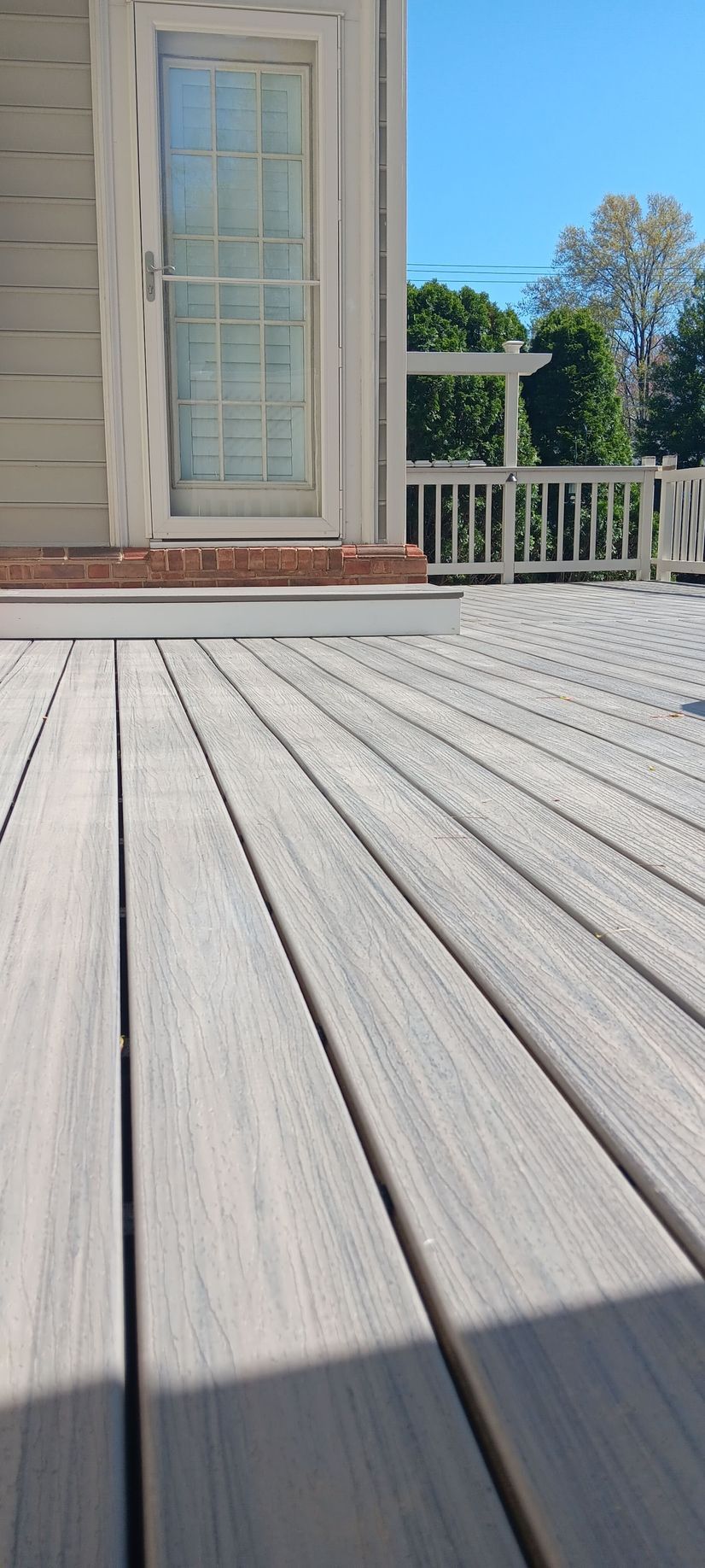 Gray deck with door and a white railing against a blue sky.