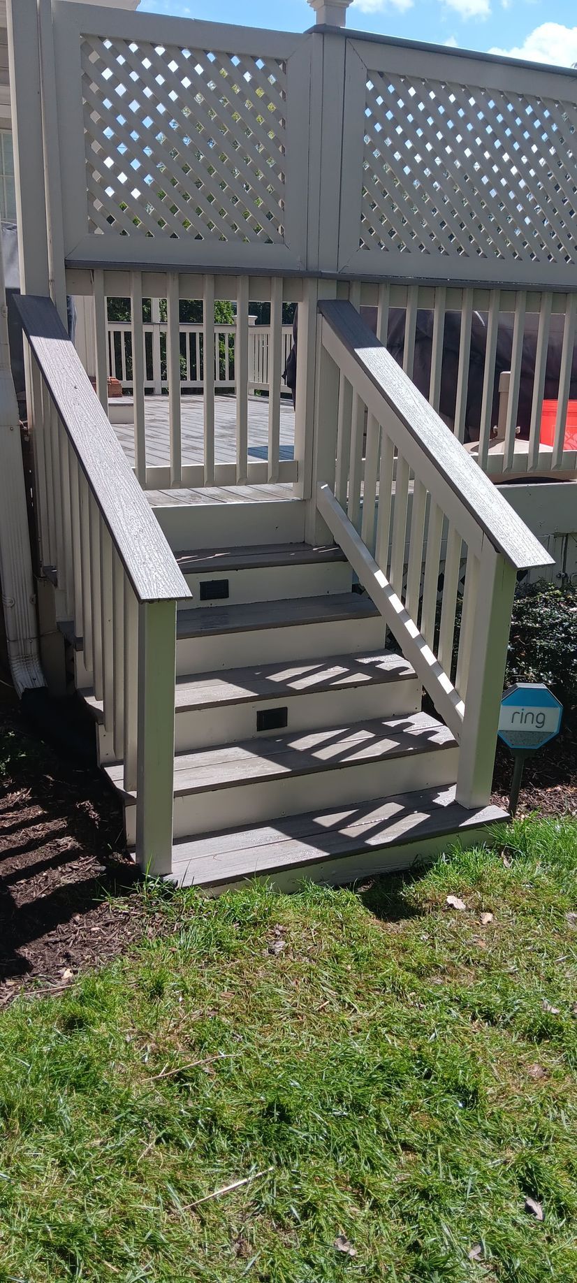 Wooden deck stairs leading to a deck with a decorative lattice railing. Green grass surrounds the steps.