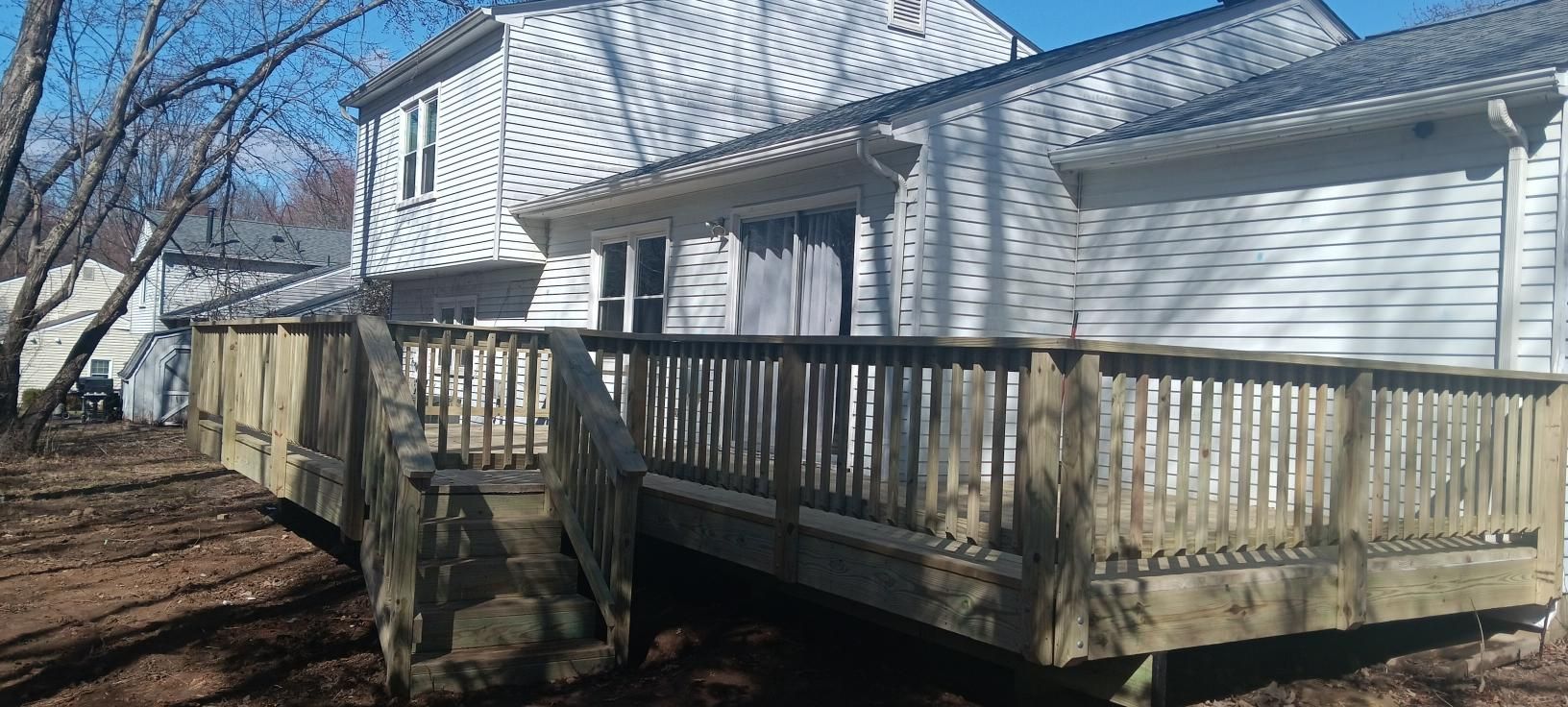 Wooden deck next to a white house with bare trees and a blue sky.