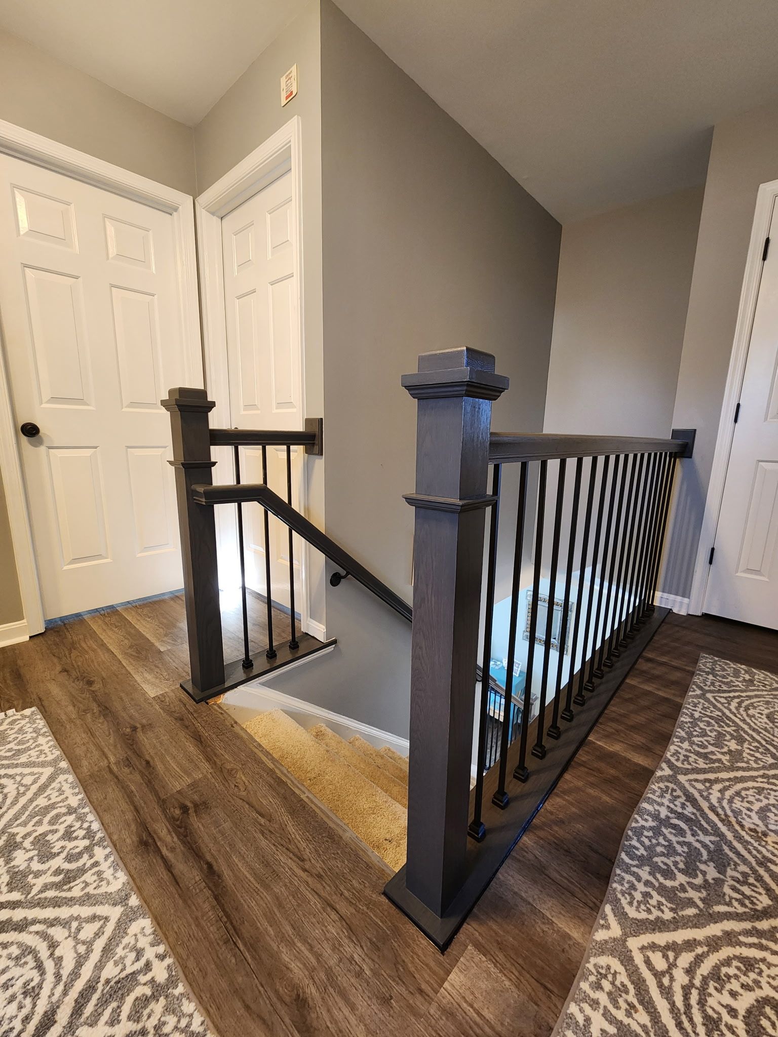 Hallway with stairs and dark gray railing. Two white doors are on the left and right.