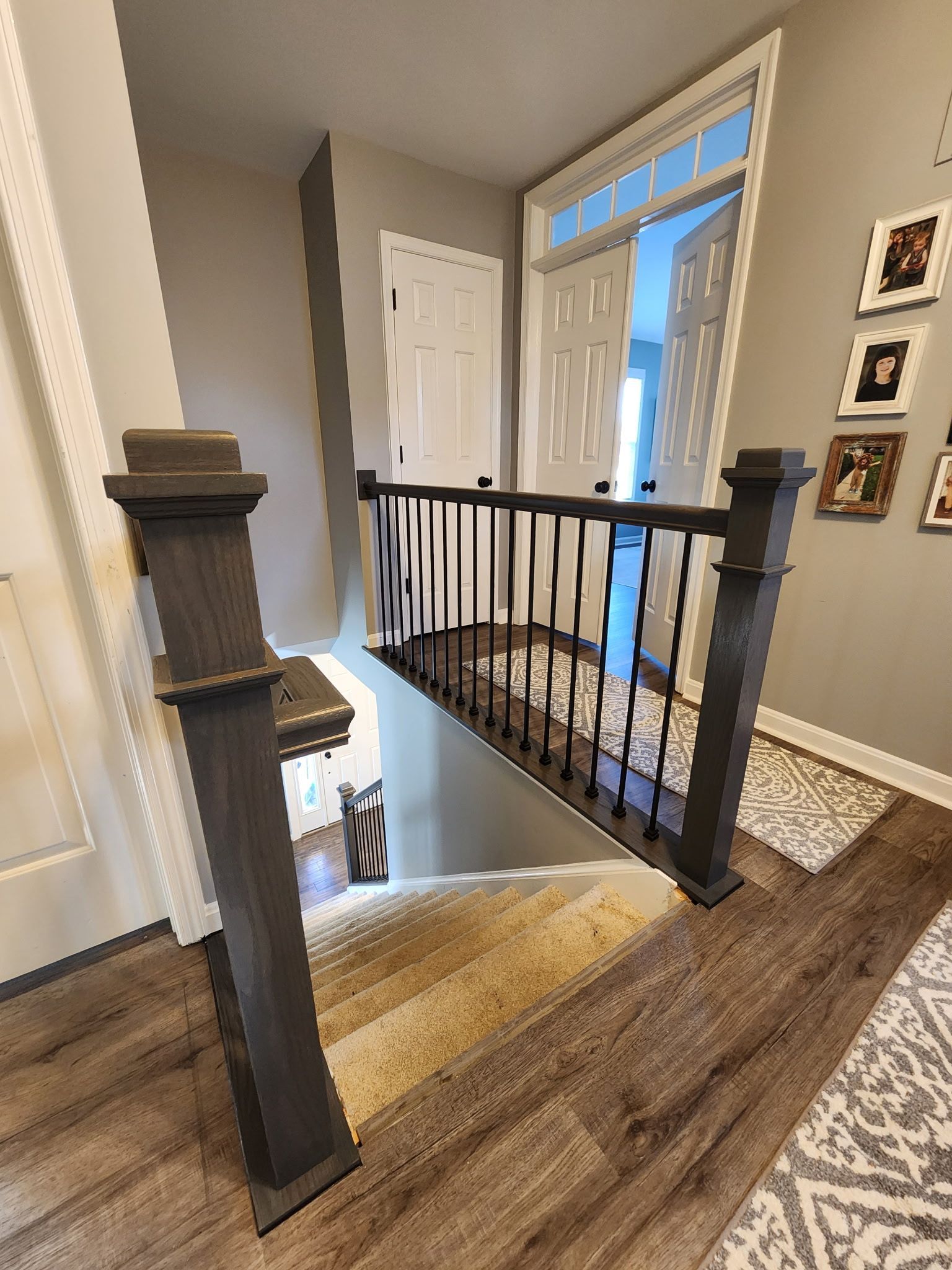 Staircase with wooden steps, dark gray posts, and black iron railings. Light wood-look flooring. Door and entryway visible.