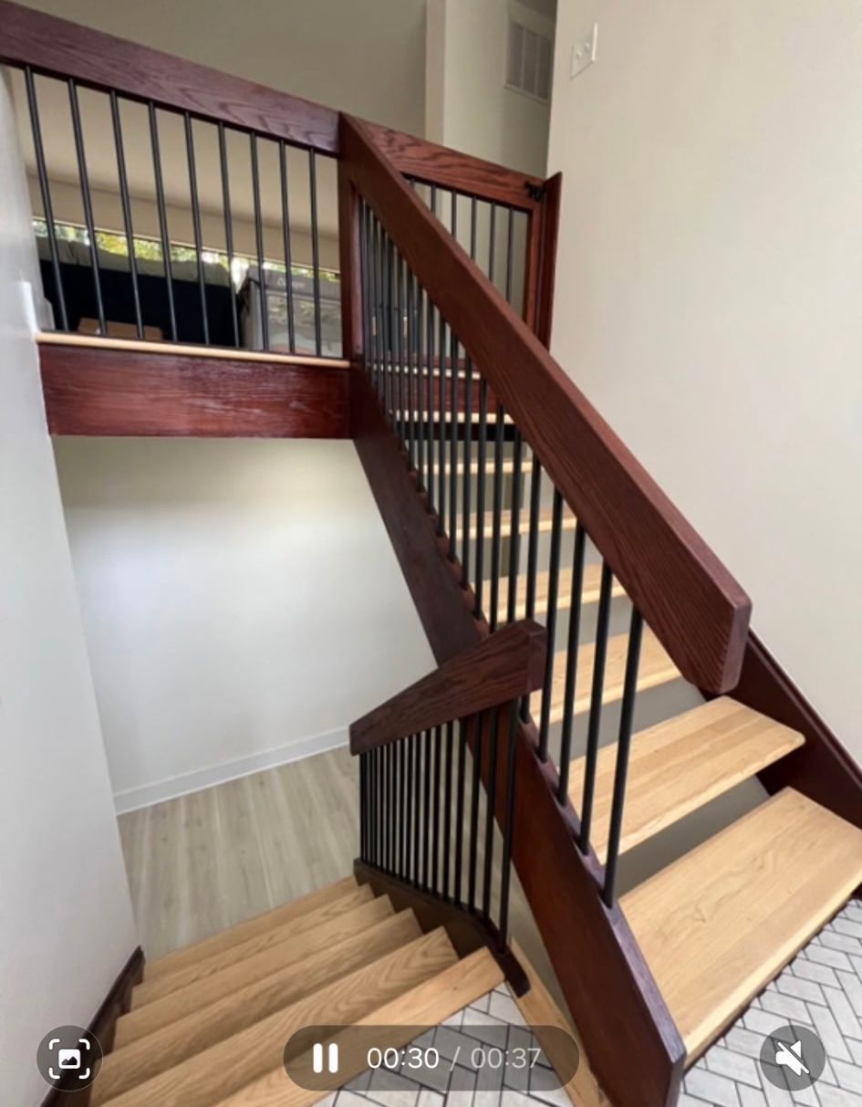 Wooden staircase with dark brown handrails and black metal balusters. Light colored stairs. Beige walls.
