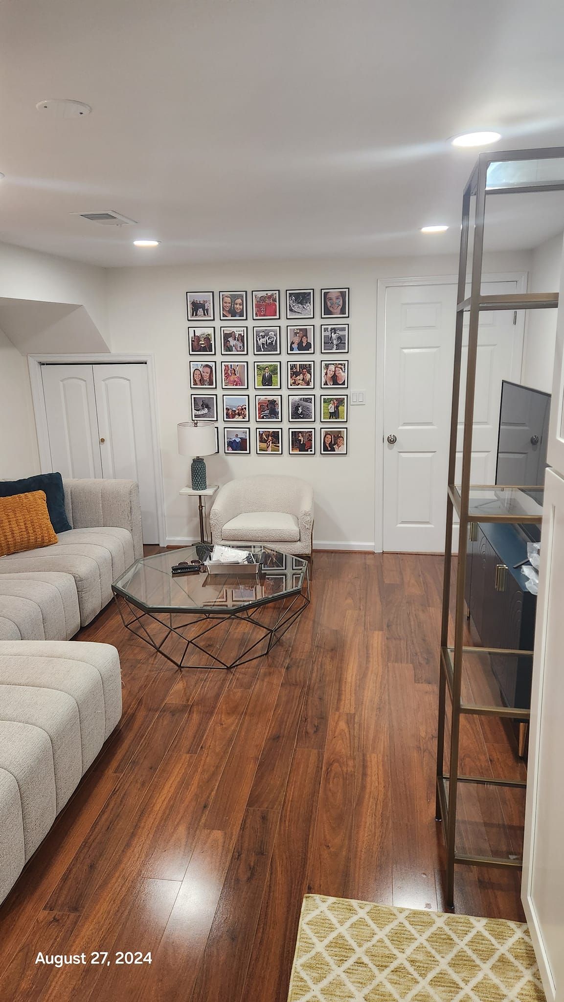 Living room with hardwood floors, a couch, chair, and photo display on the wall.