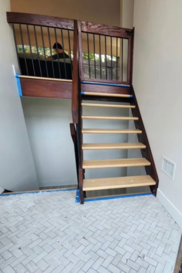 Staircase with wooden steps and railing, leading up to a landing. White and gray tiled floor.