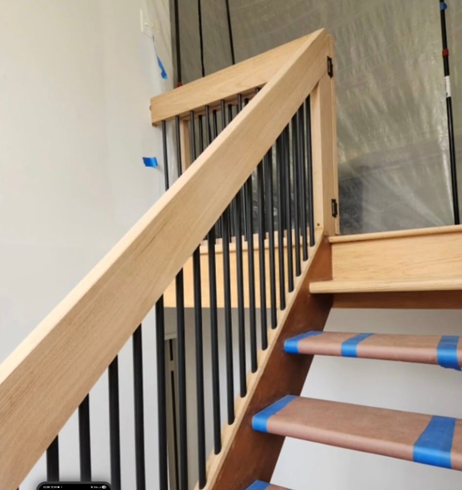 Wooden staircase with black metal balusters and protective tape on the steps.