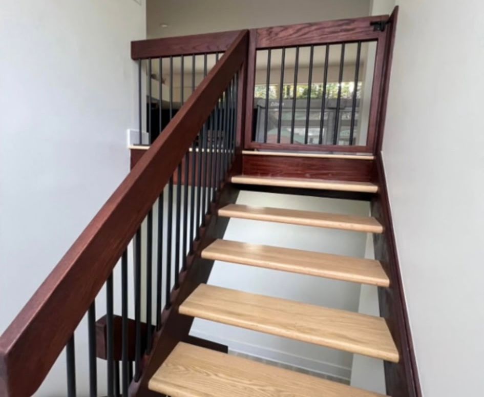 Wooden staircase with a gate at the top. The stairs are light colored with dark brown railings and black vertical bars.