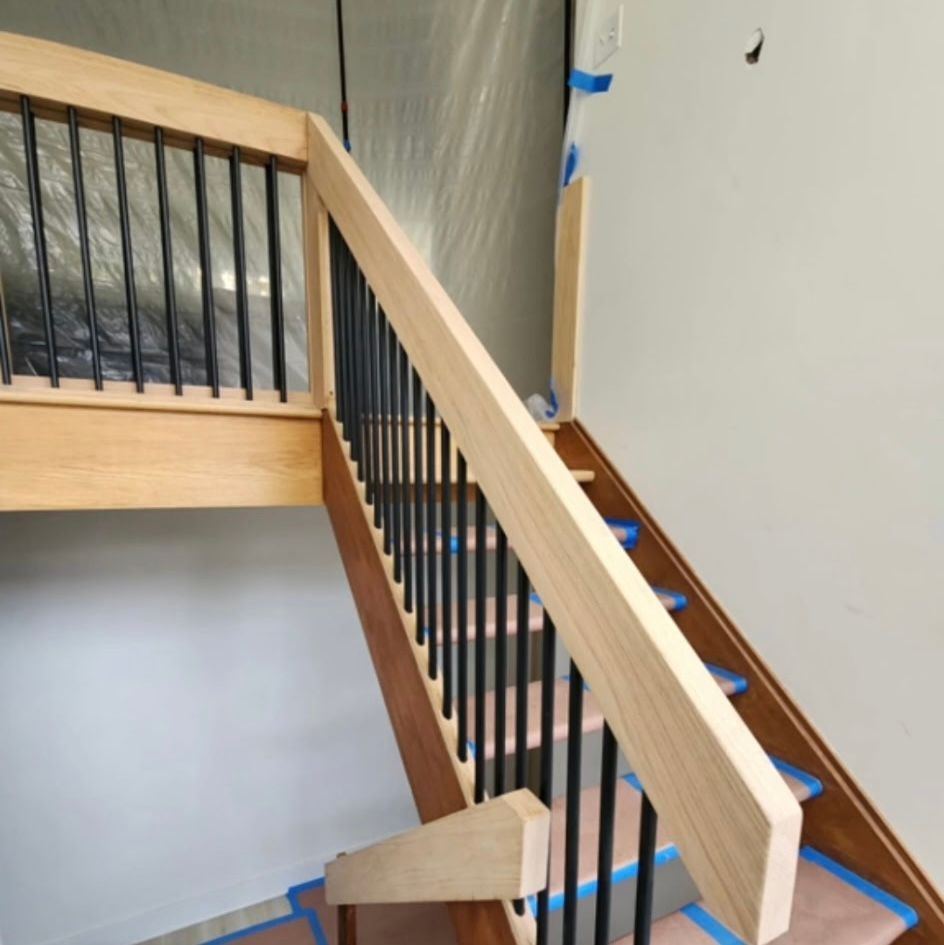 Wooden staircase with black metal balusters and light-colored handrail, under construction.