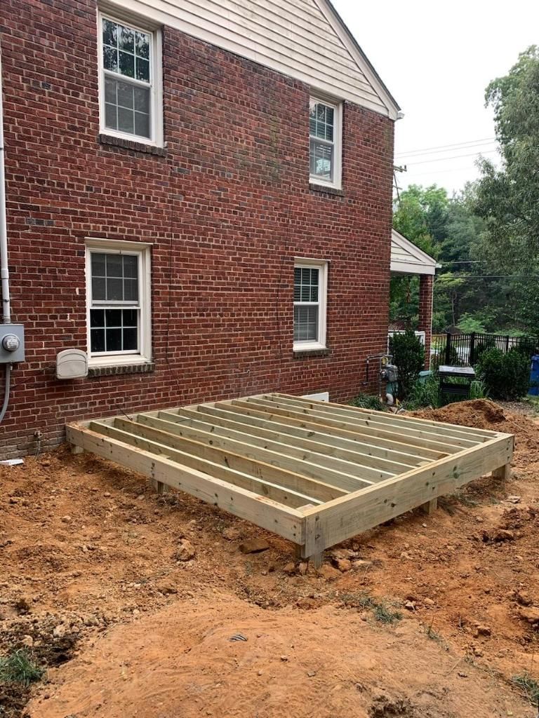 A wooden deck is being built in front of a brick house.