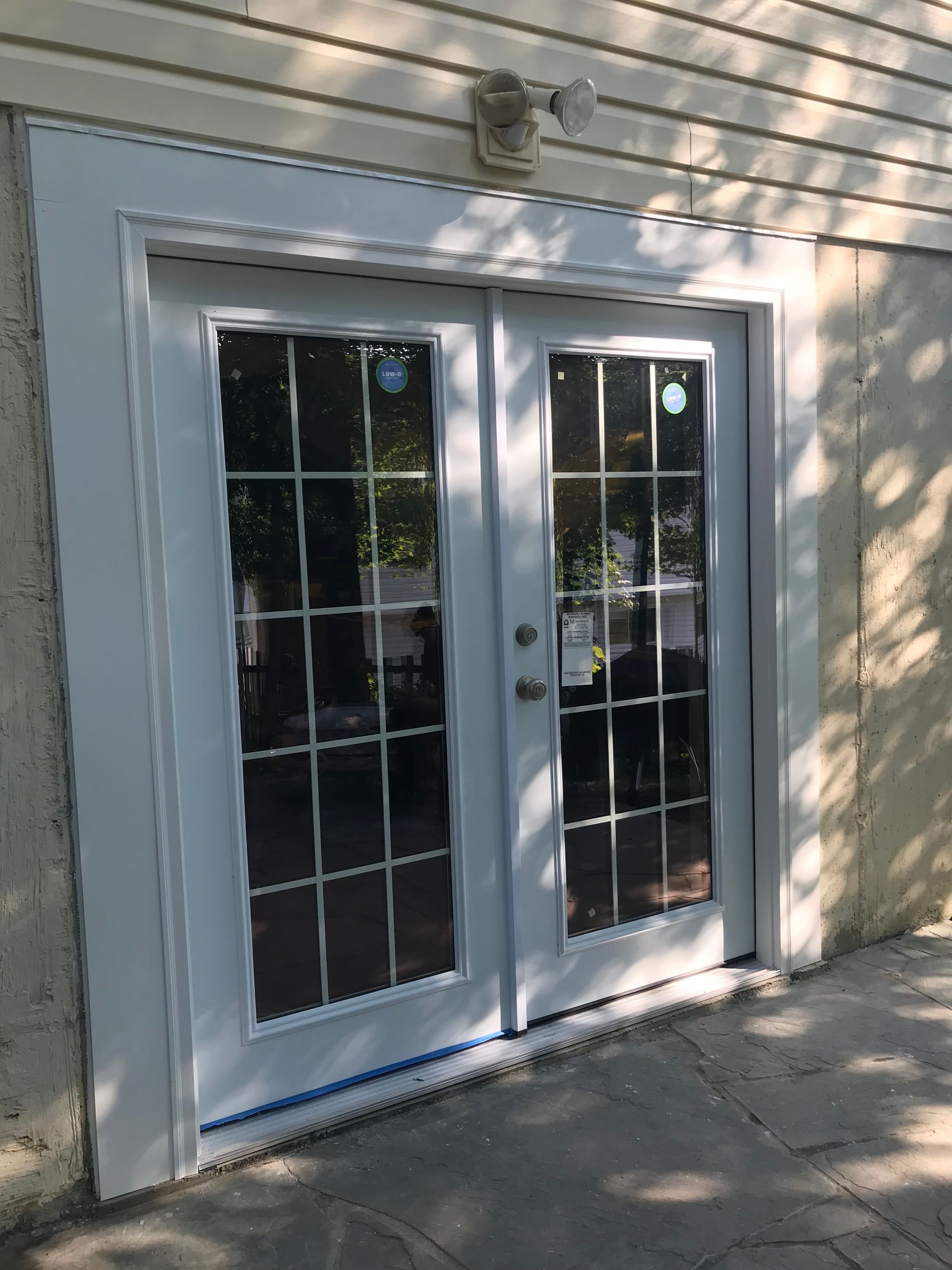 Double white glass doors with white trim, and a security light fixture, on a beige building exterior.