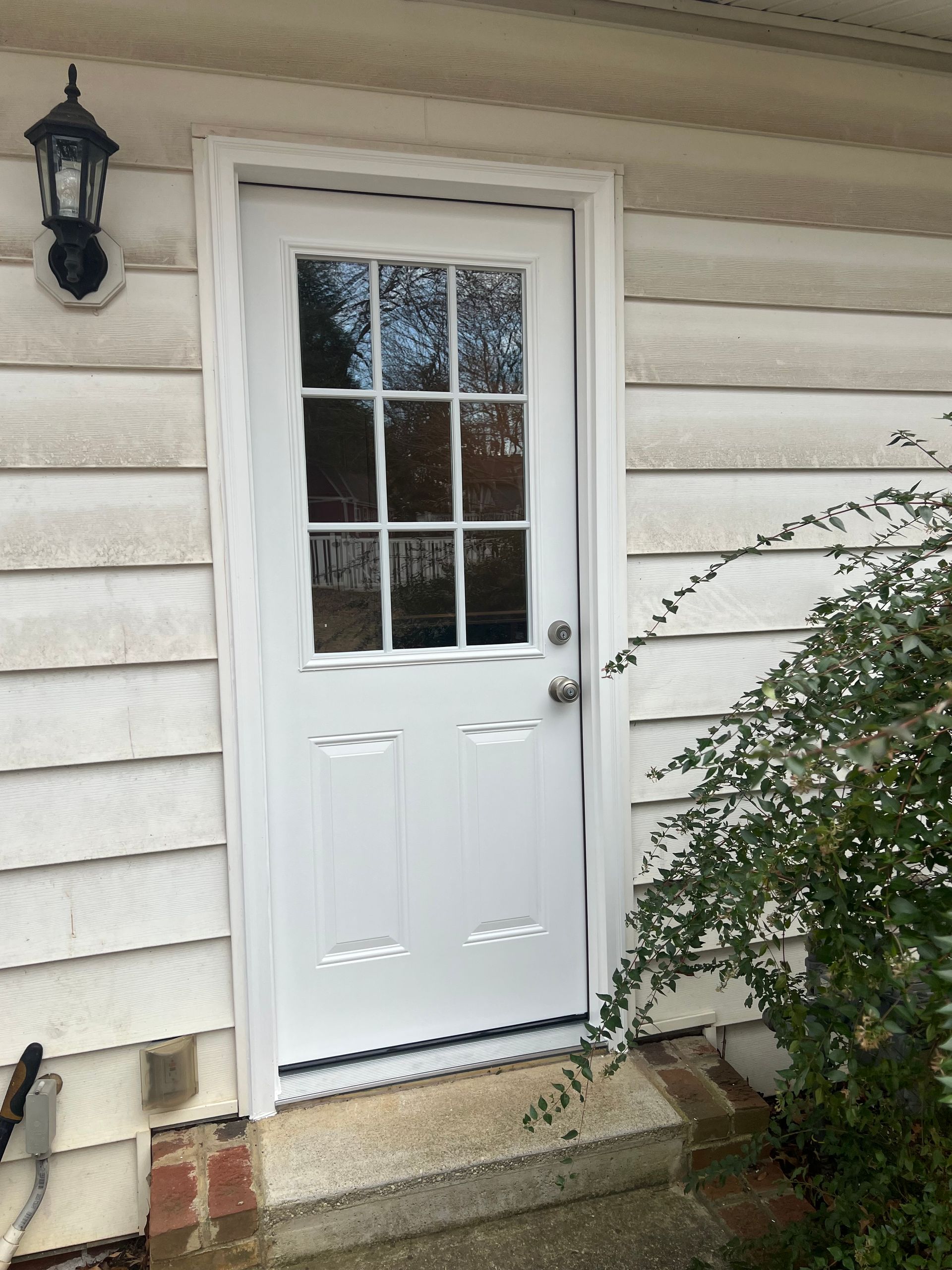 White exterior door with glass panes, framed by white trim, on a light-colored building with a step.
