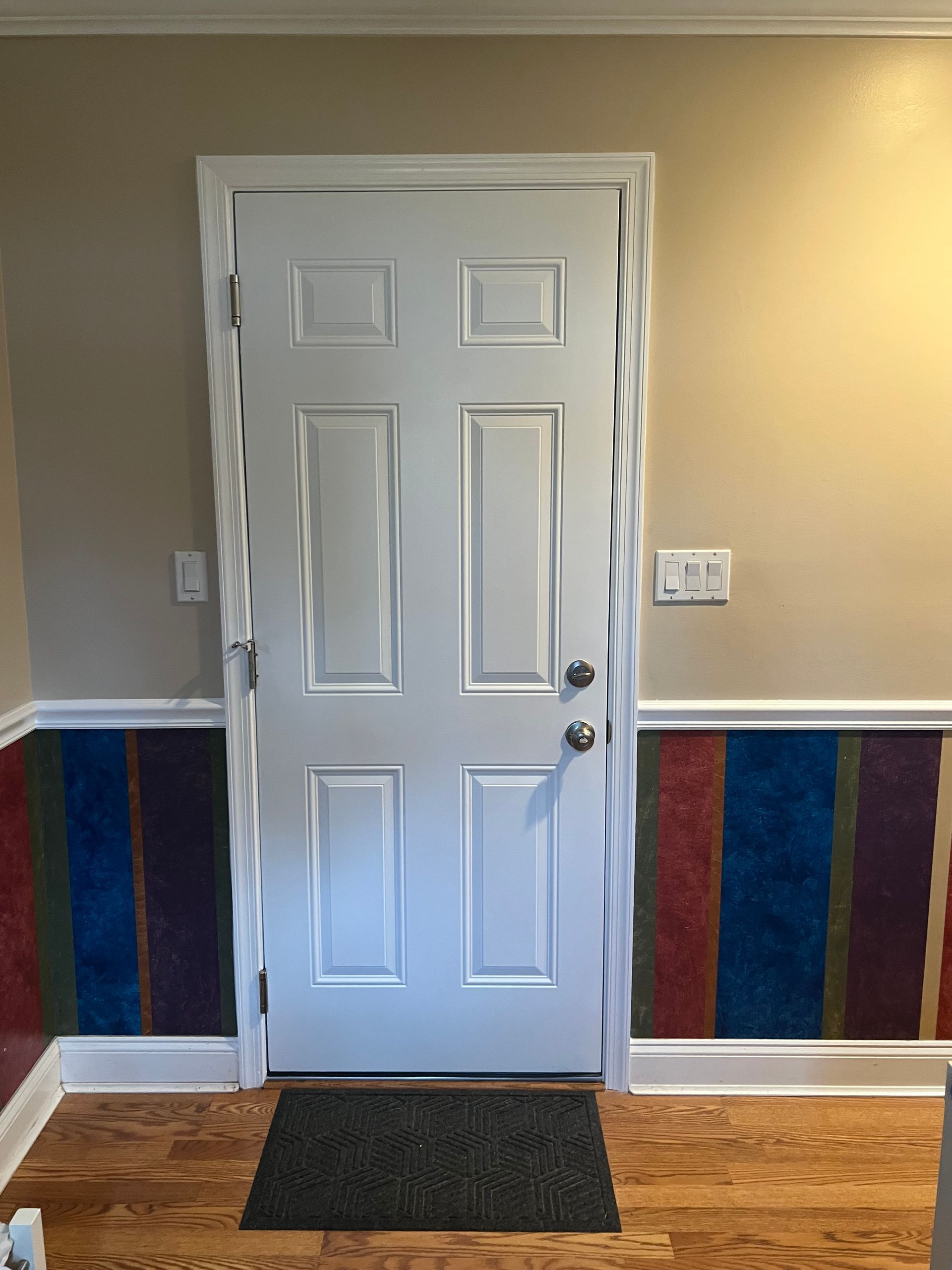 White door centered on a wall with colorful stripes and light beige paint.