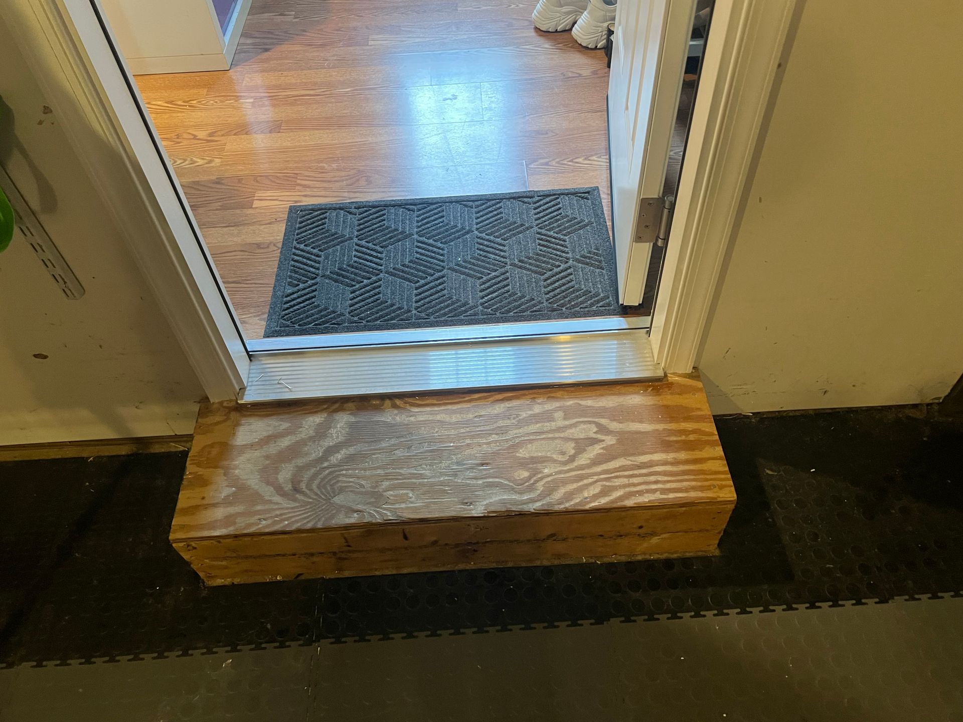 Wooden step platform at a doorway with a mat inside.