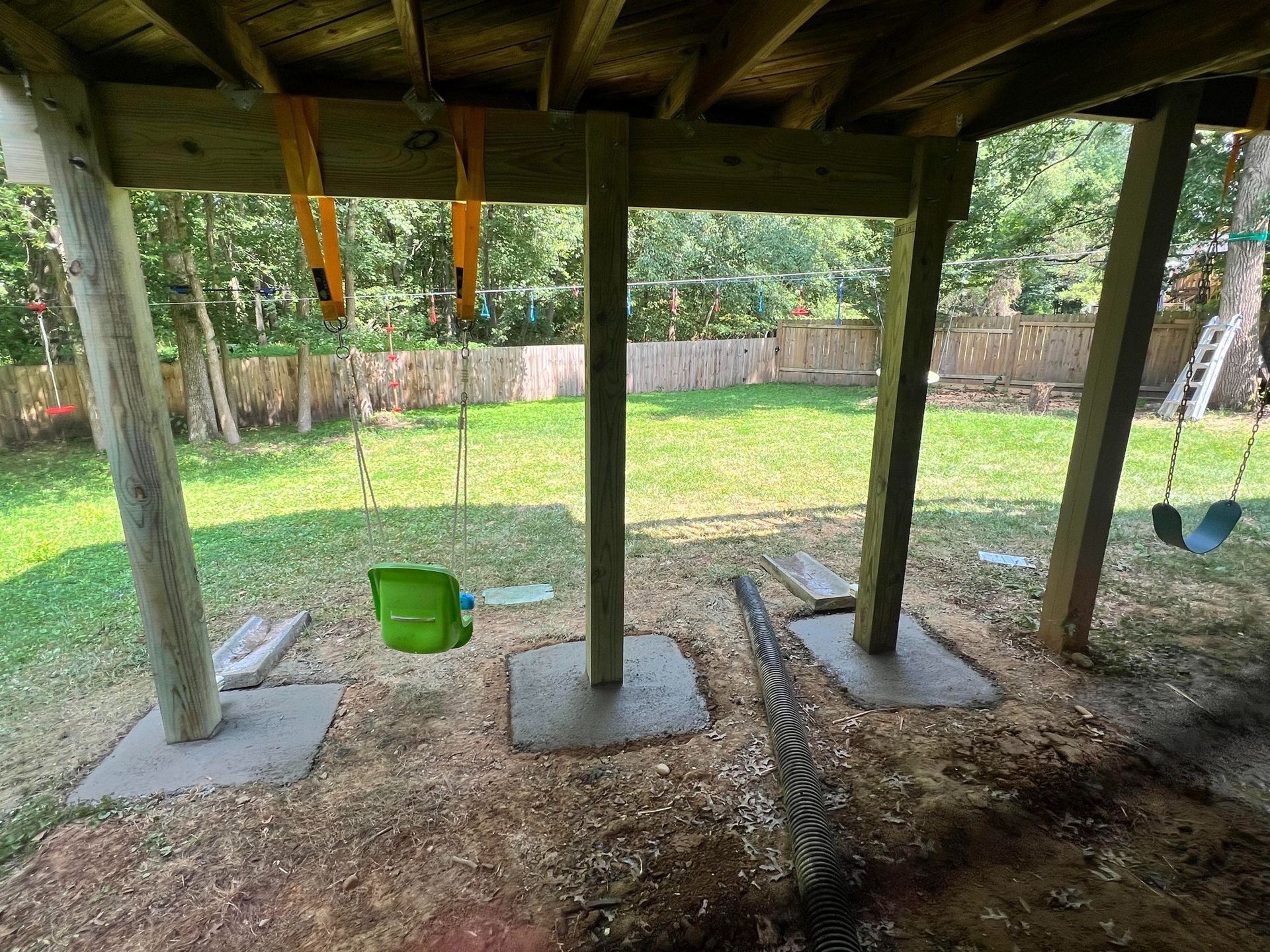 A wooden deck with swings underneath it in a backyard.