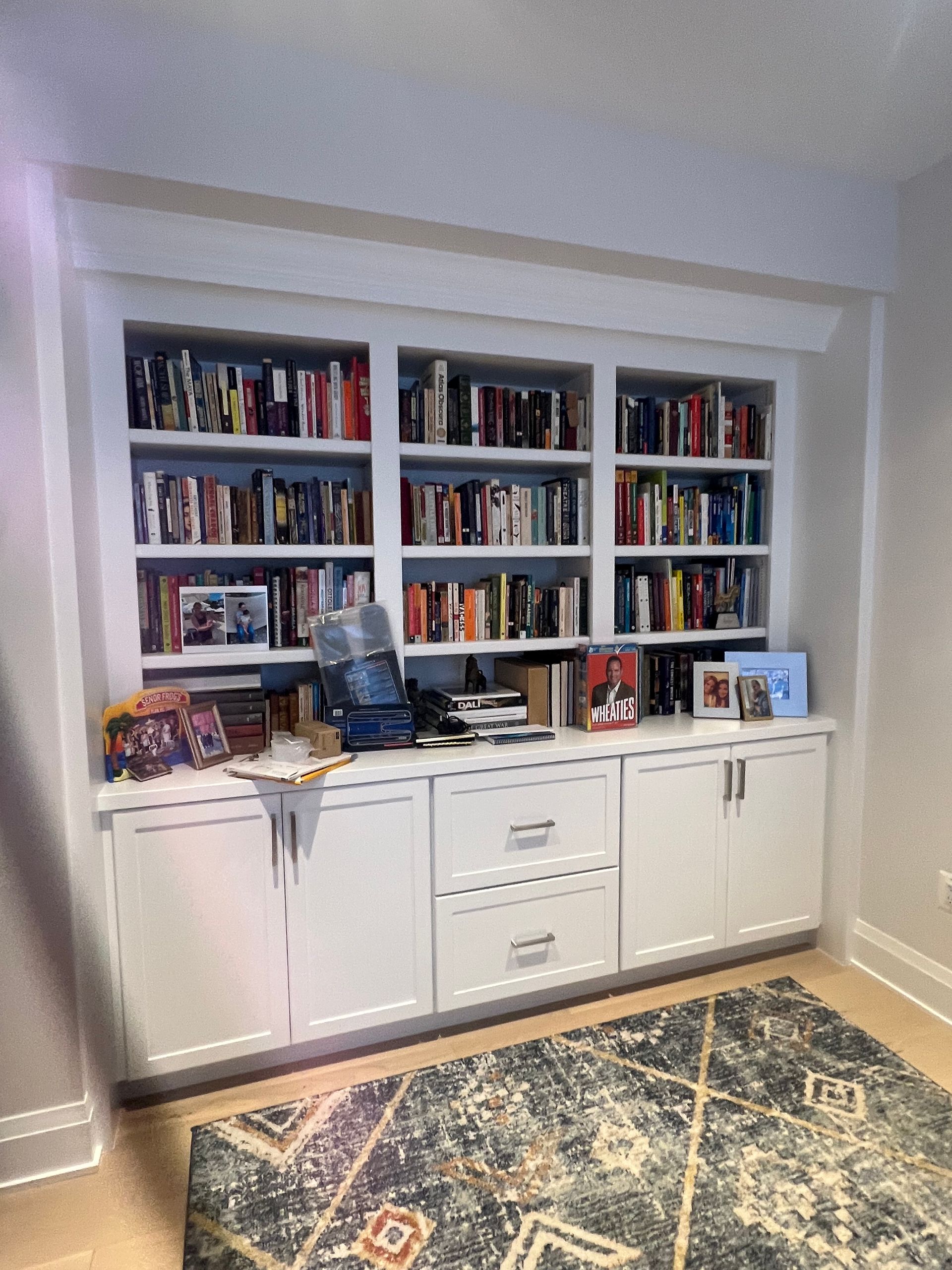 White built-in bookcase filled with books, drawers, and cabinet doors, above a rug.