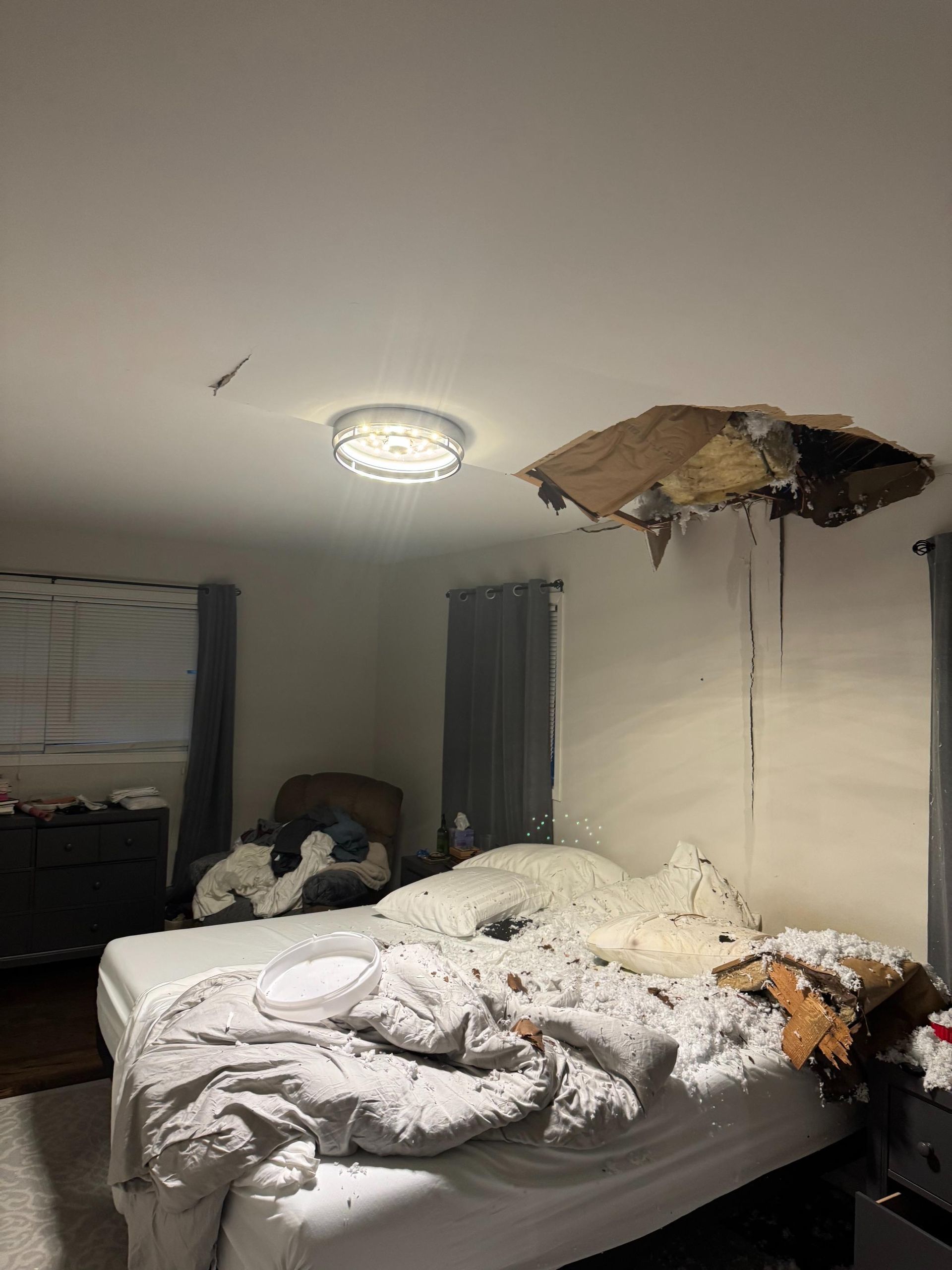 Bedroom ceiling collapsed above bed, debris strewn about. Ceiling light intact.