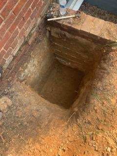 A hole in the ground next to a brick wall.