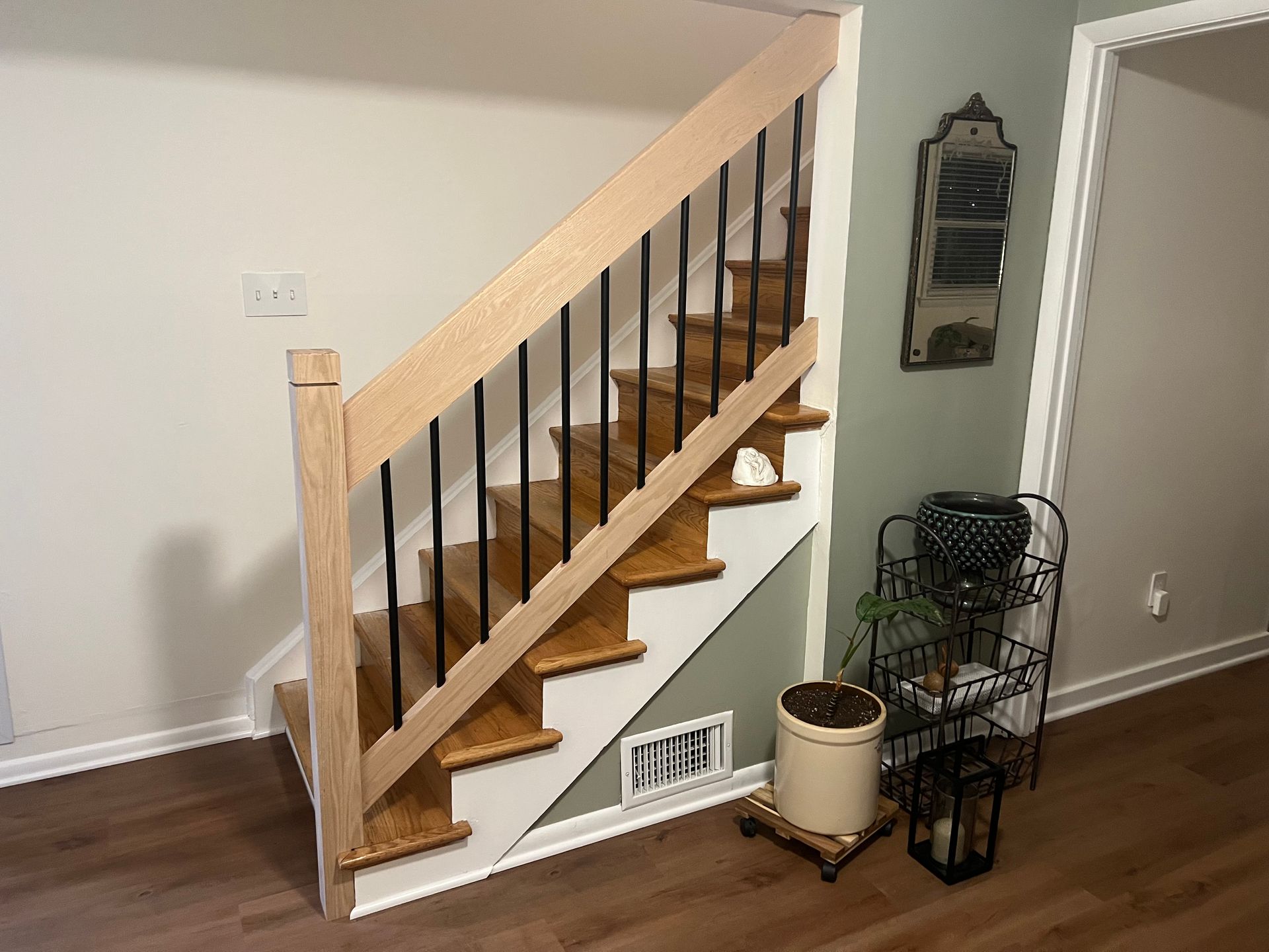 Staircase with wooden steps and railing, black balusters, white trim, on a hardwood floor.