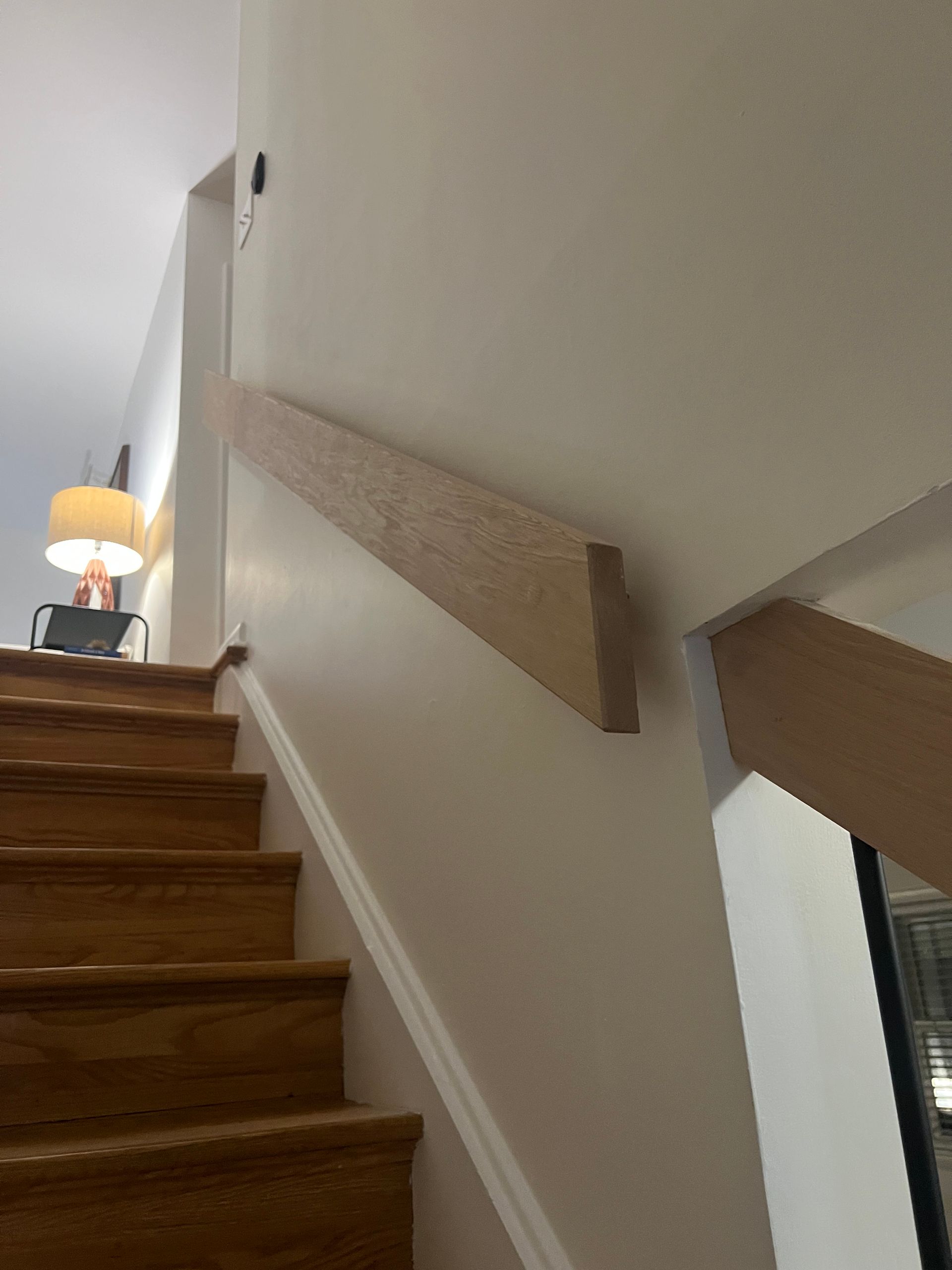 Wooden handrail on a white wall next to a staircase.