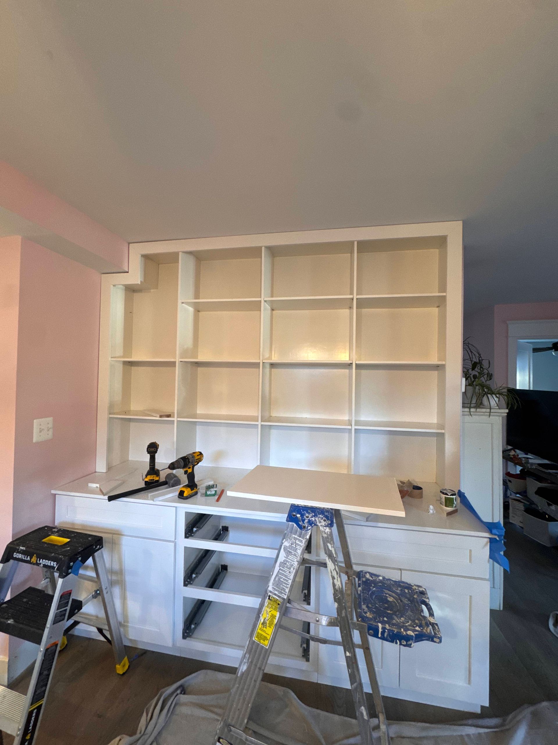 White built-in shelving unit under construction in a room. Tools and materials are on the cabinets.