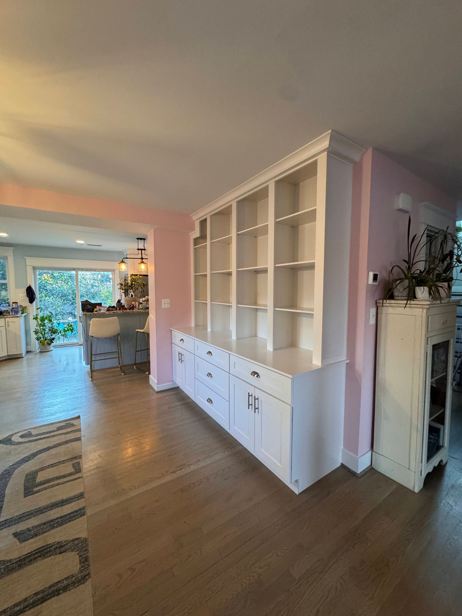 White built-in shelving and cabinets against a pale pink wall in a home with hardwood floors.