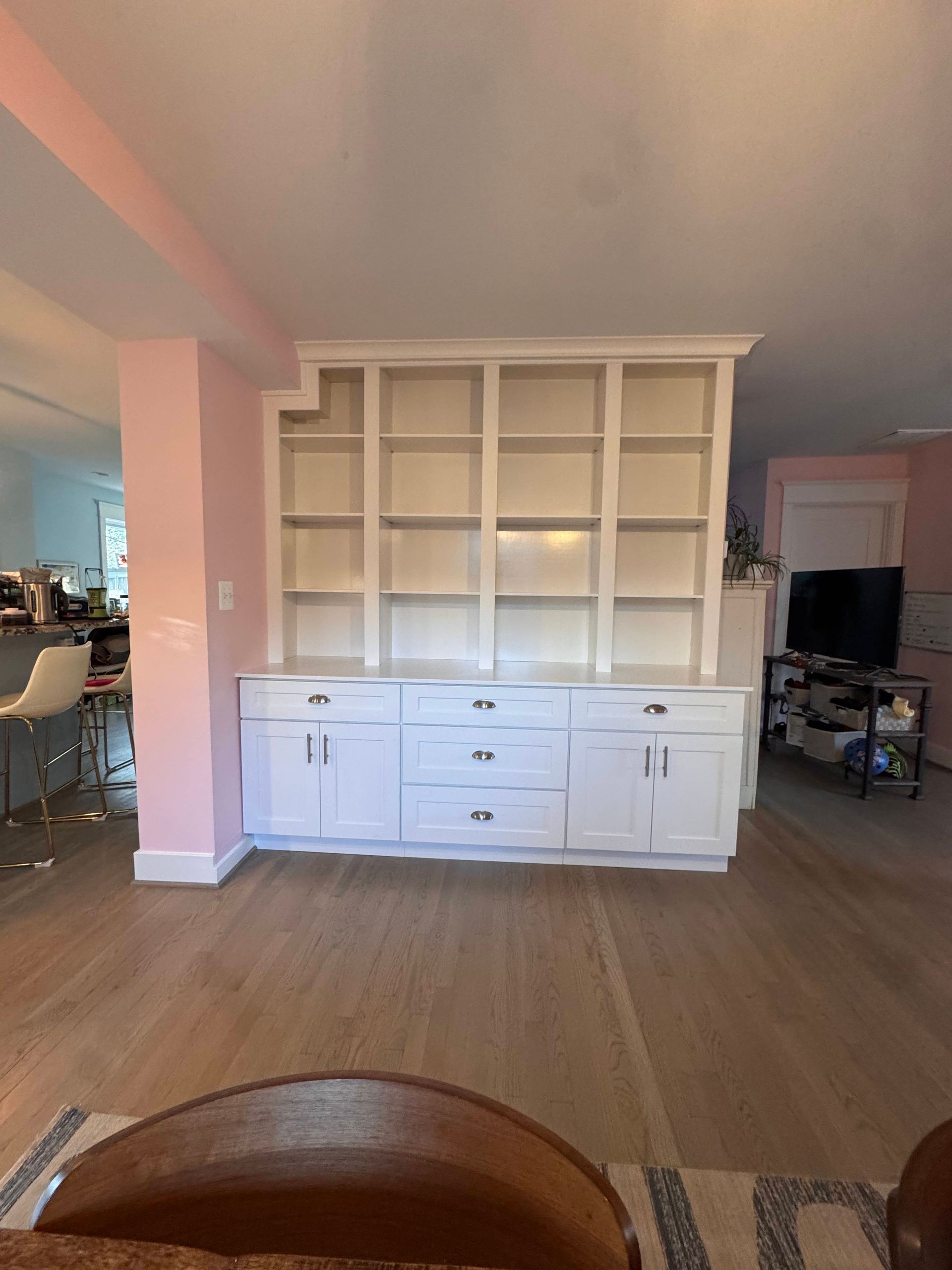 White built-in shelving unit with cabinets, centered against pink wall, in a room with hardwood floors.