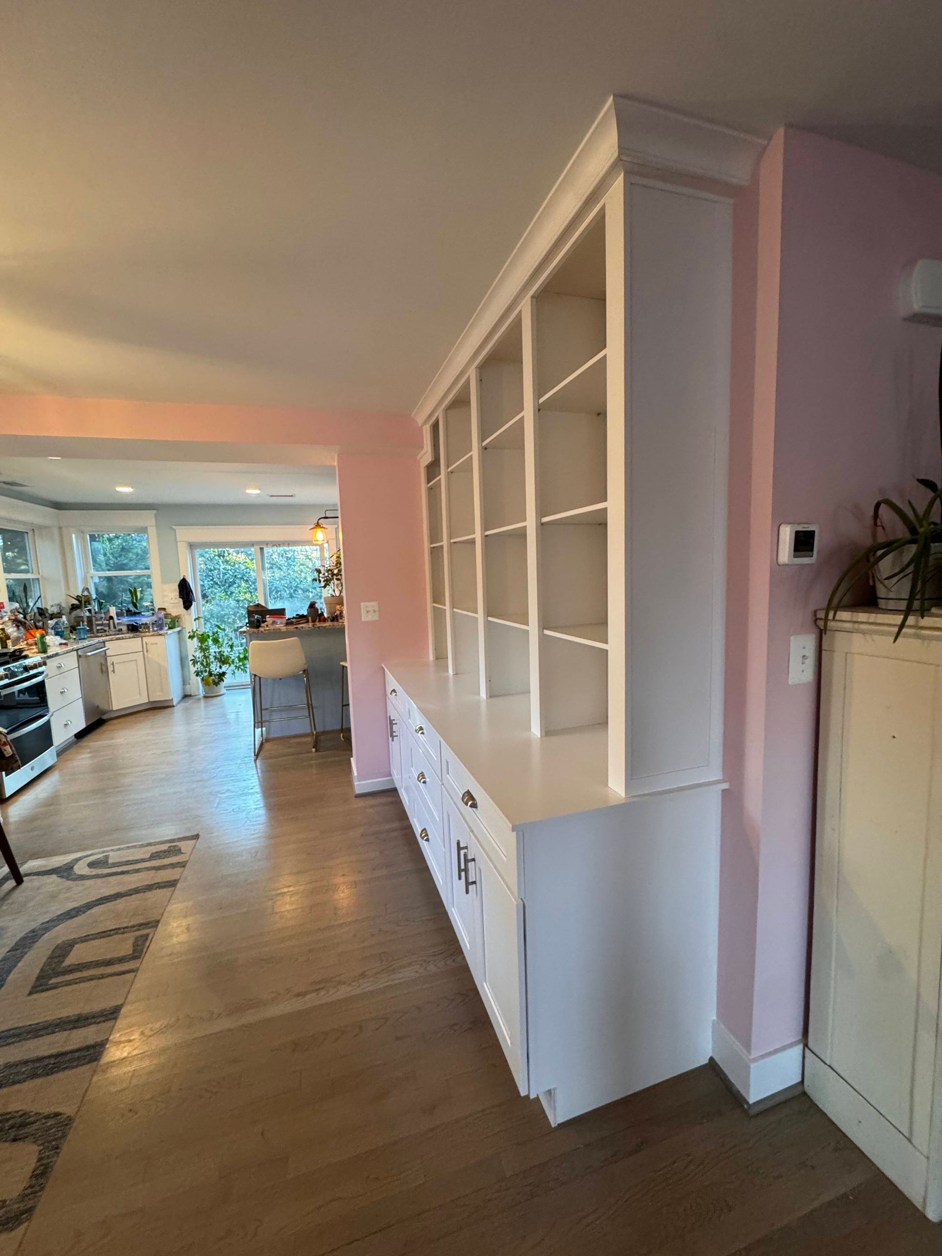 White built-in cabinet with open shelves and drawers against a pink wall in a home.