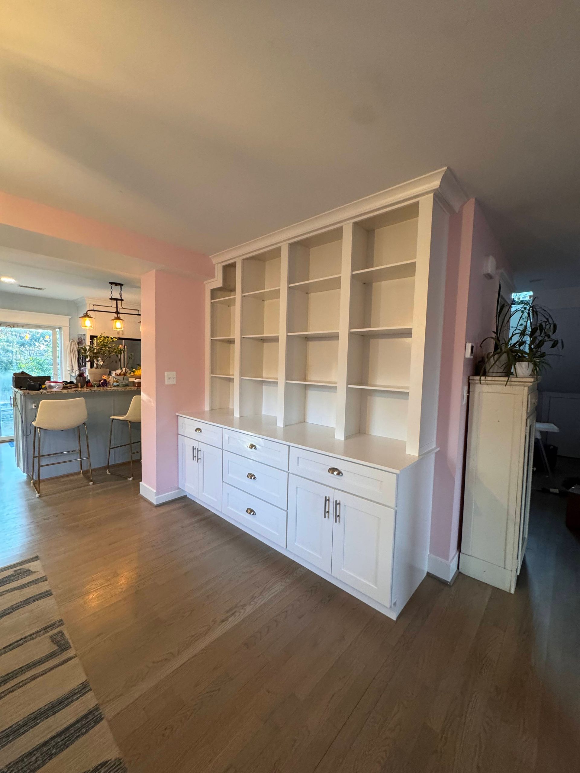 White built-in shelving unit with drawers and cabinets against a pink wall in a home.