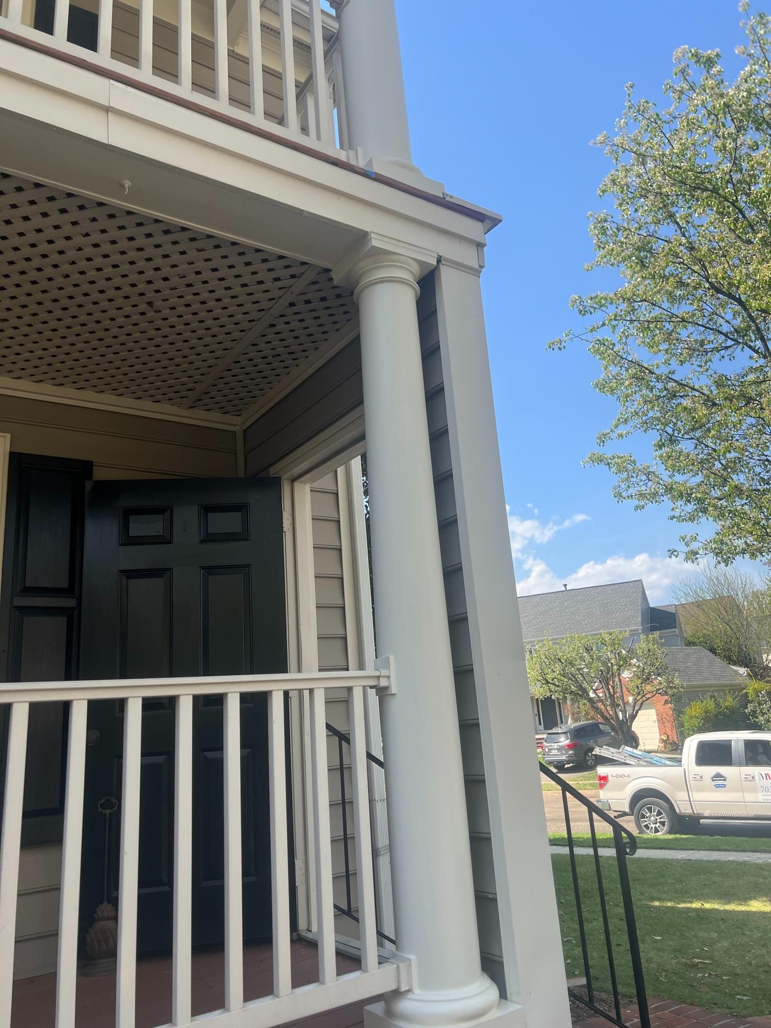 A white porch column on a house with dark gray siding, a black door, and a white lattice ceiling.