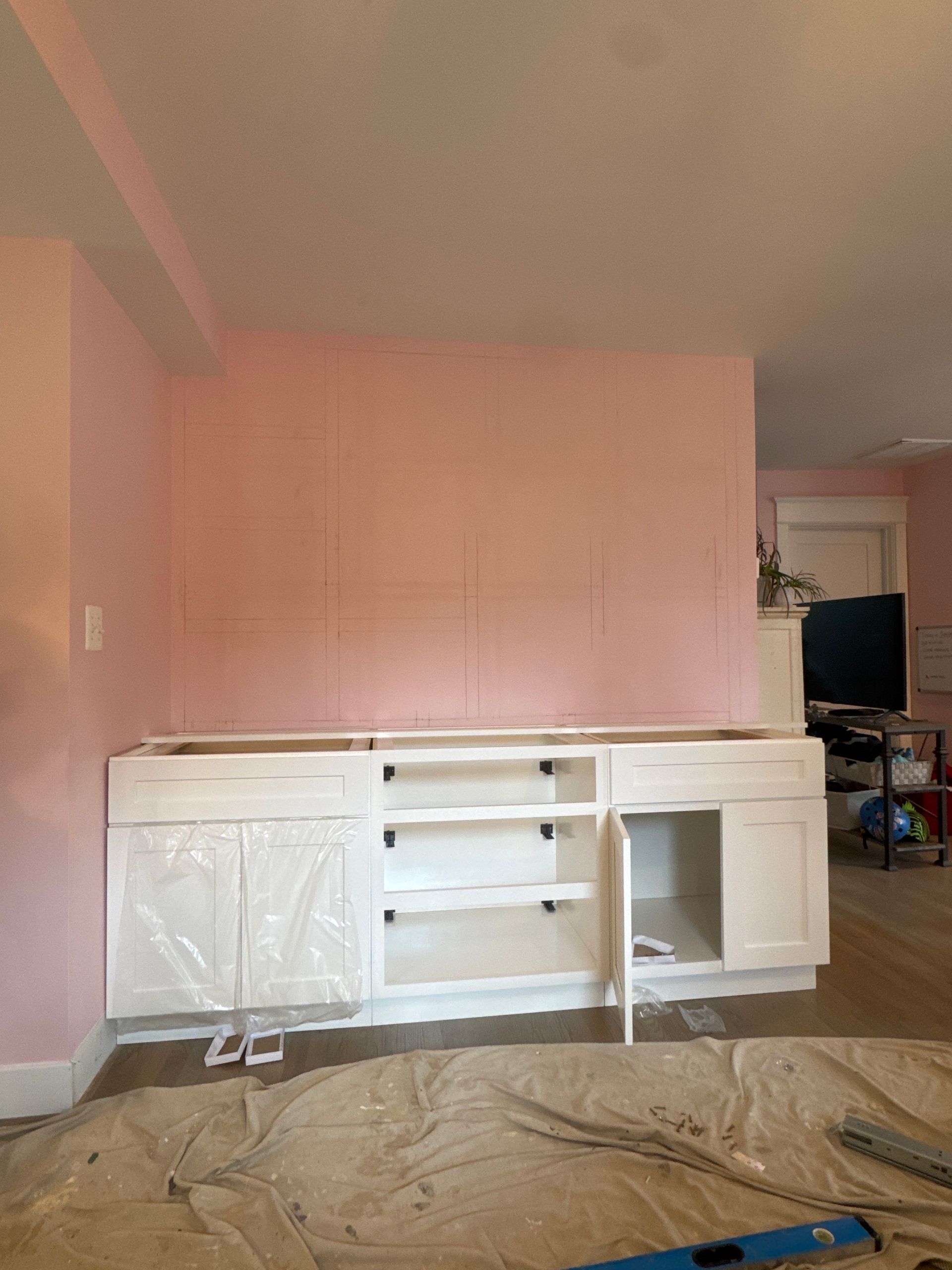 White cabinets being installed against a pink wall. A room is under renovation.