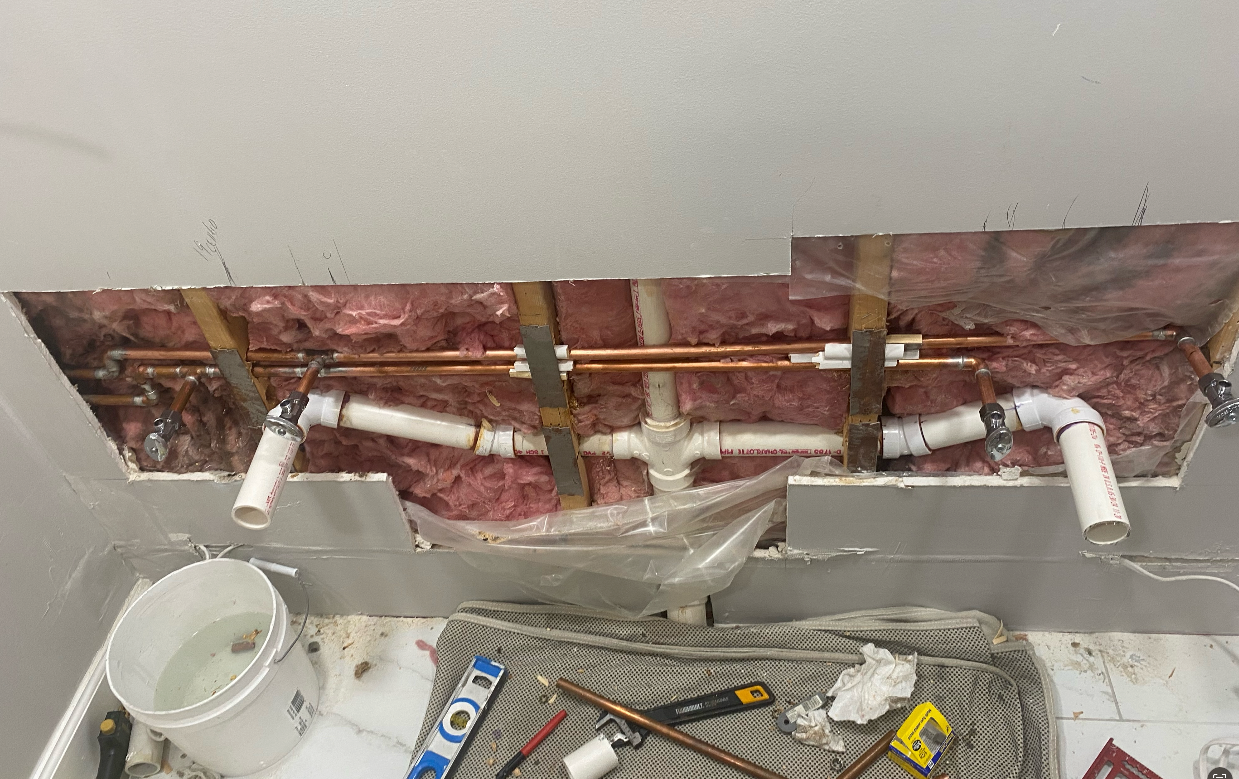 A bathroom with a hole in the wall and pipes coming out of it.