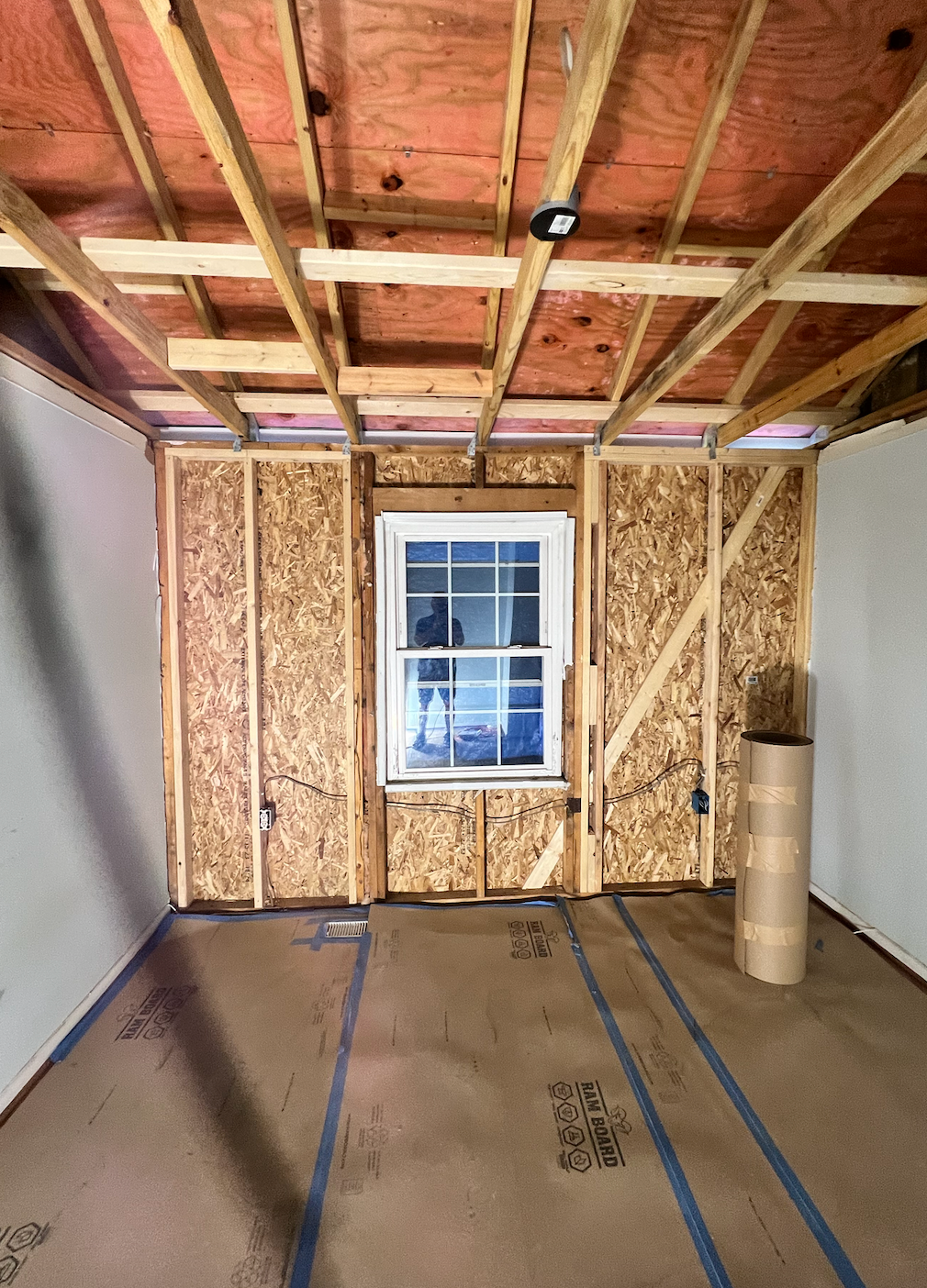 A room under construction with a window and a roll of insulation.