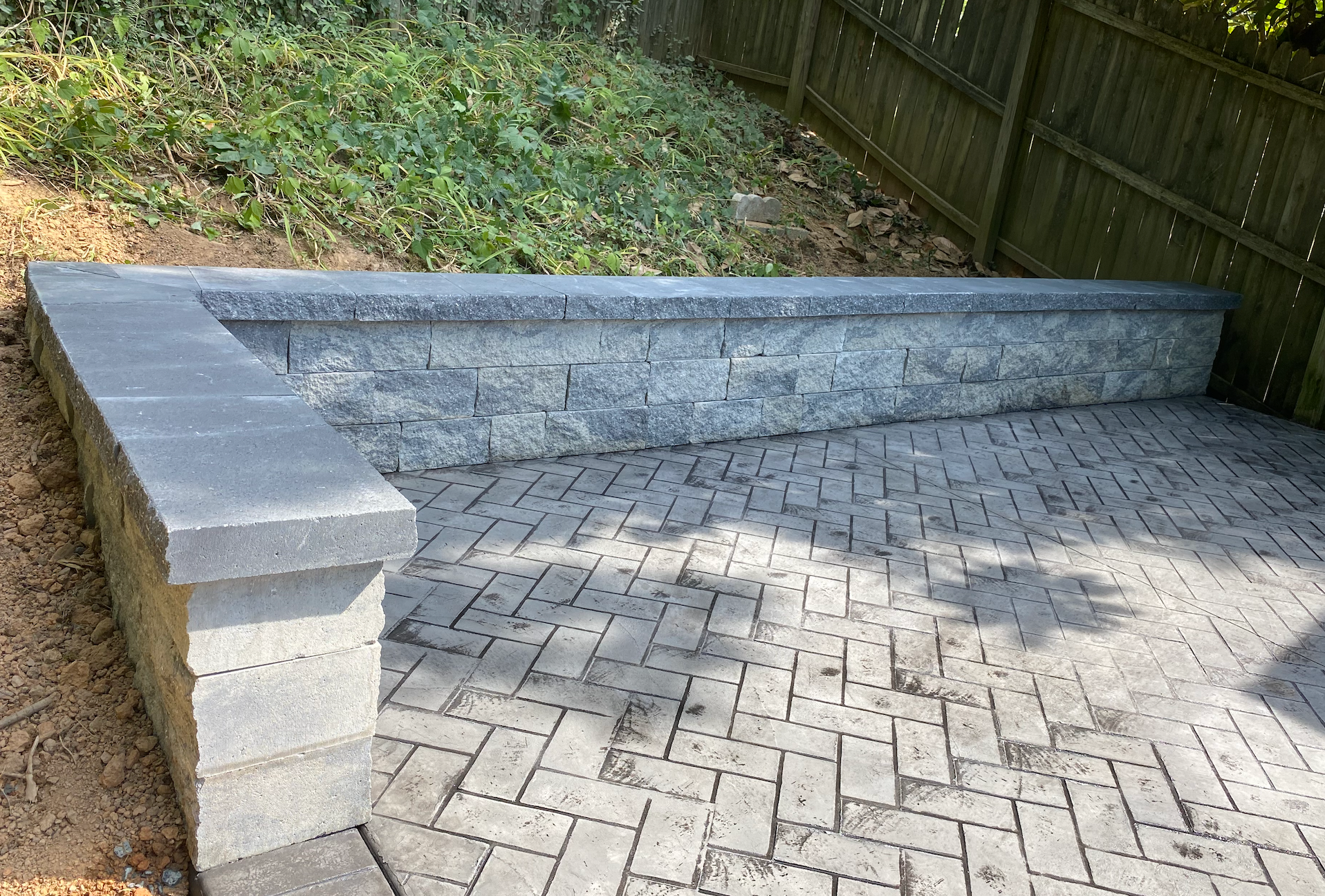 A stone wall is sitting on top of a brick patio next to a wooden fence.