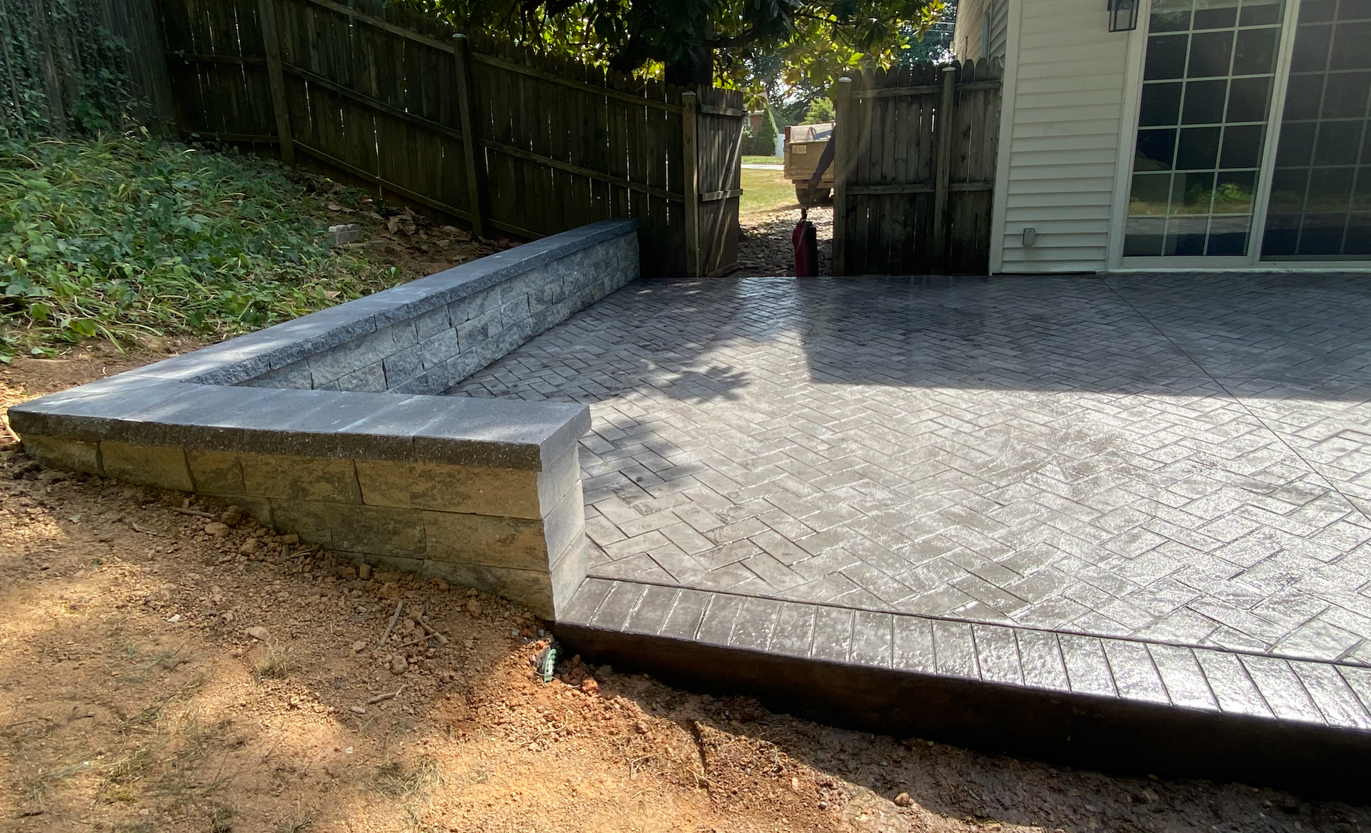 A patio with a bench and a fence in the backyard of a house.