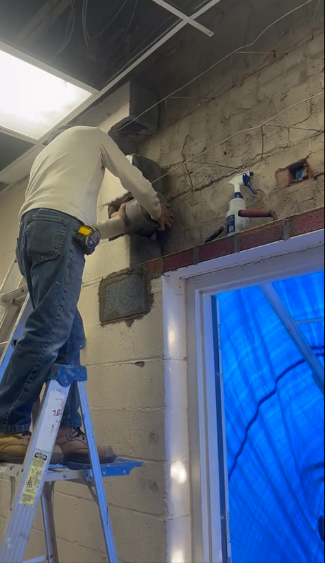 A man is standing on a ladder working on a wall.
