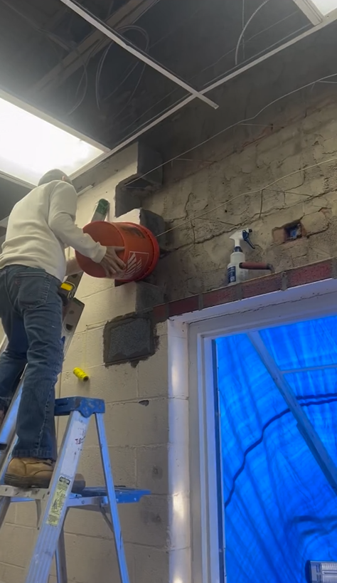 A man is standing on a ladder working on a wall.