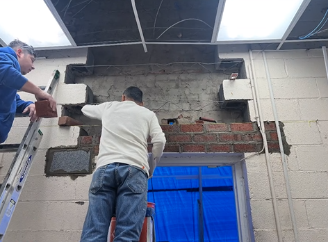 Two men standing on a ladder working on a brick wall
