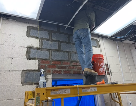 A man is standing on a ladder in front of a brick wall.